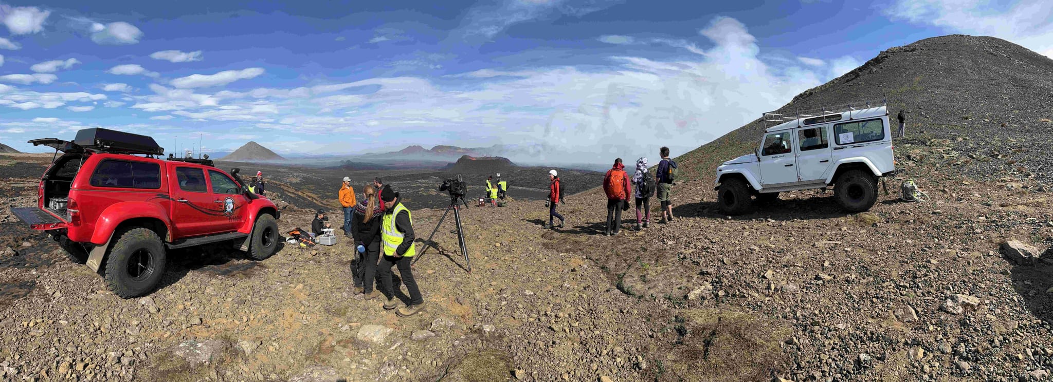 Two off-road vehicles parked in a rugged landscape, and a group of people scattered 