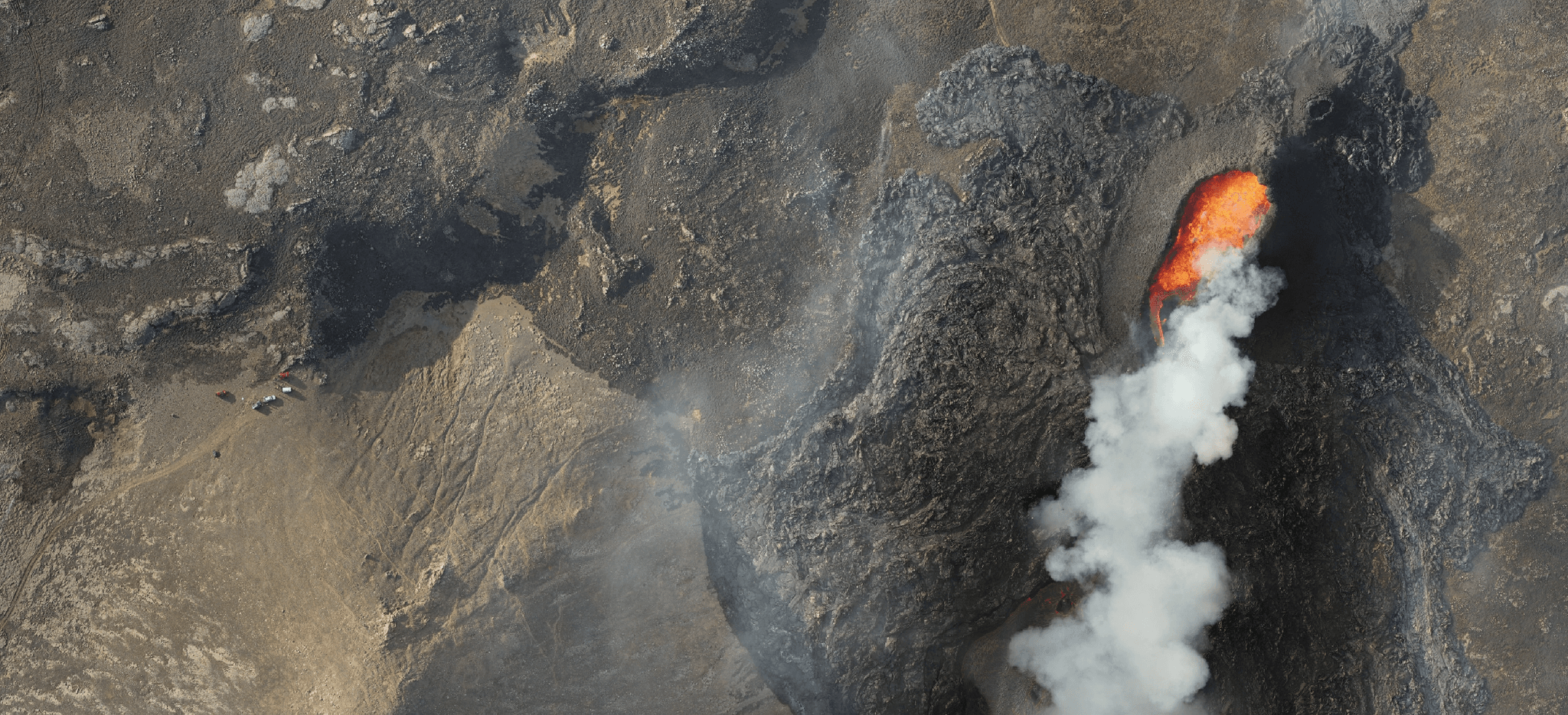 An aerial view of volcano eruption  with lava glowing orange and white smoke rising from the eruption