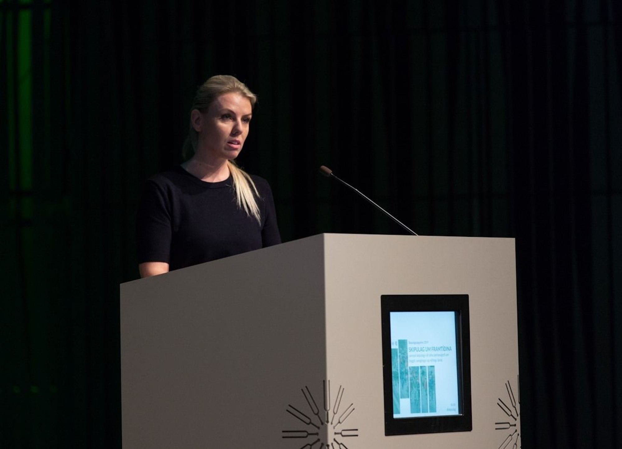 A woman standing at a podium with microphone and dark background