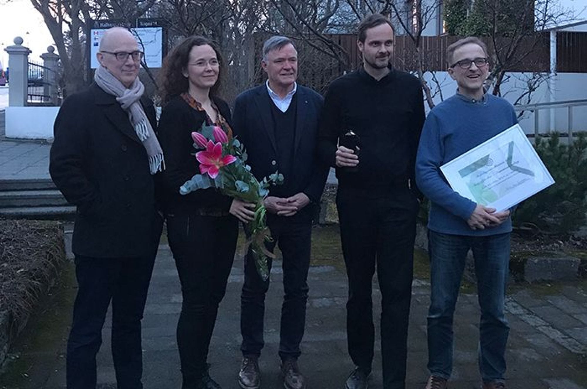 A group of people standing together, holding flowers and certificate