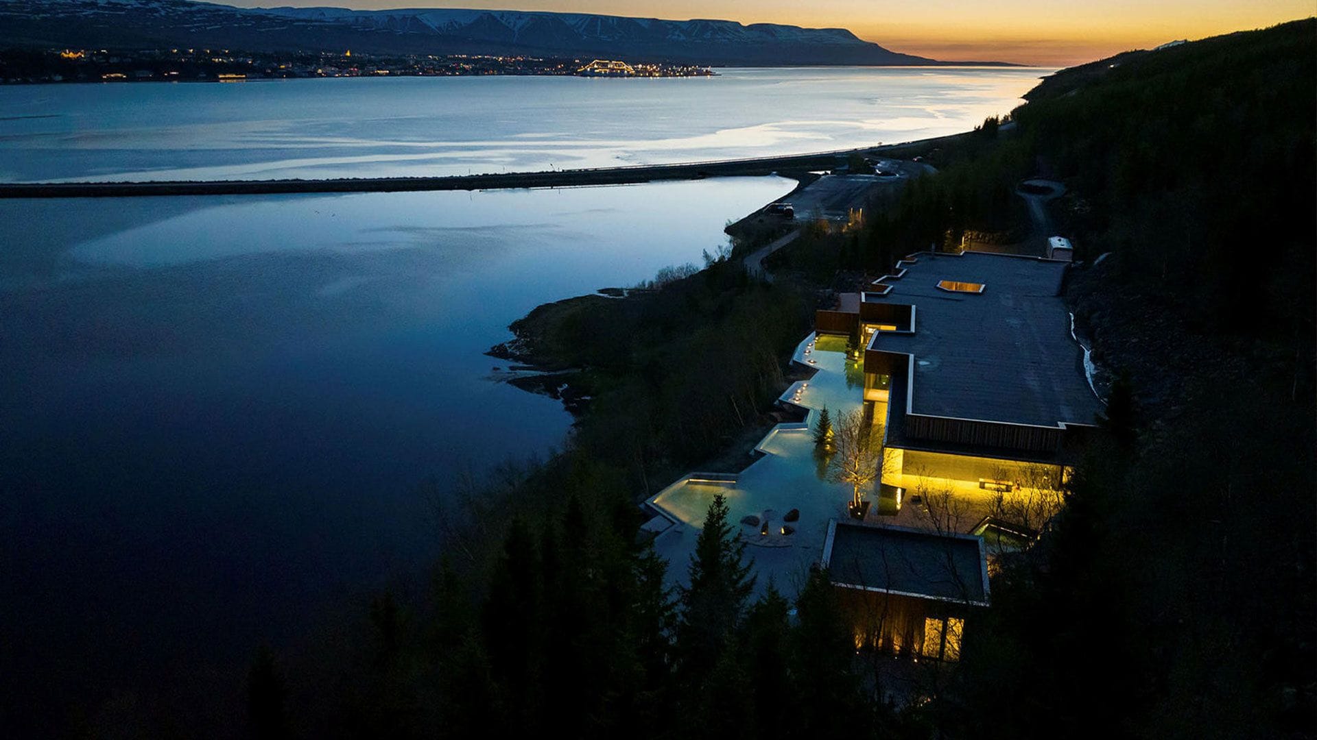 A nighttime scene of a coastal area with illuminated buildings alongside the water