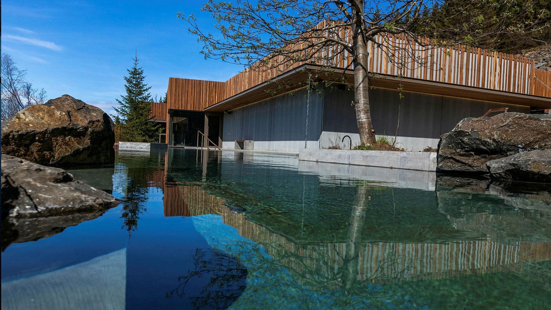 An outdoor pool with calm, clear water flanked by large rocks 