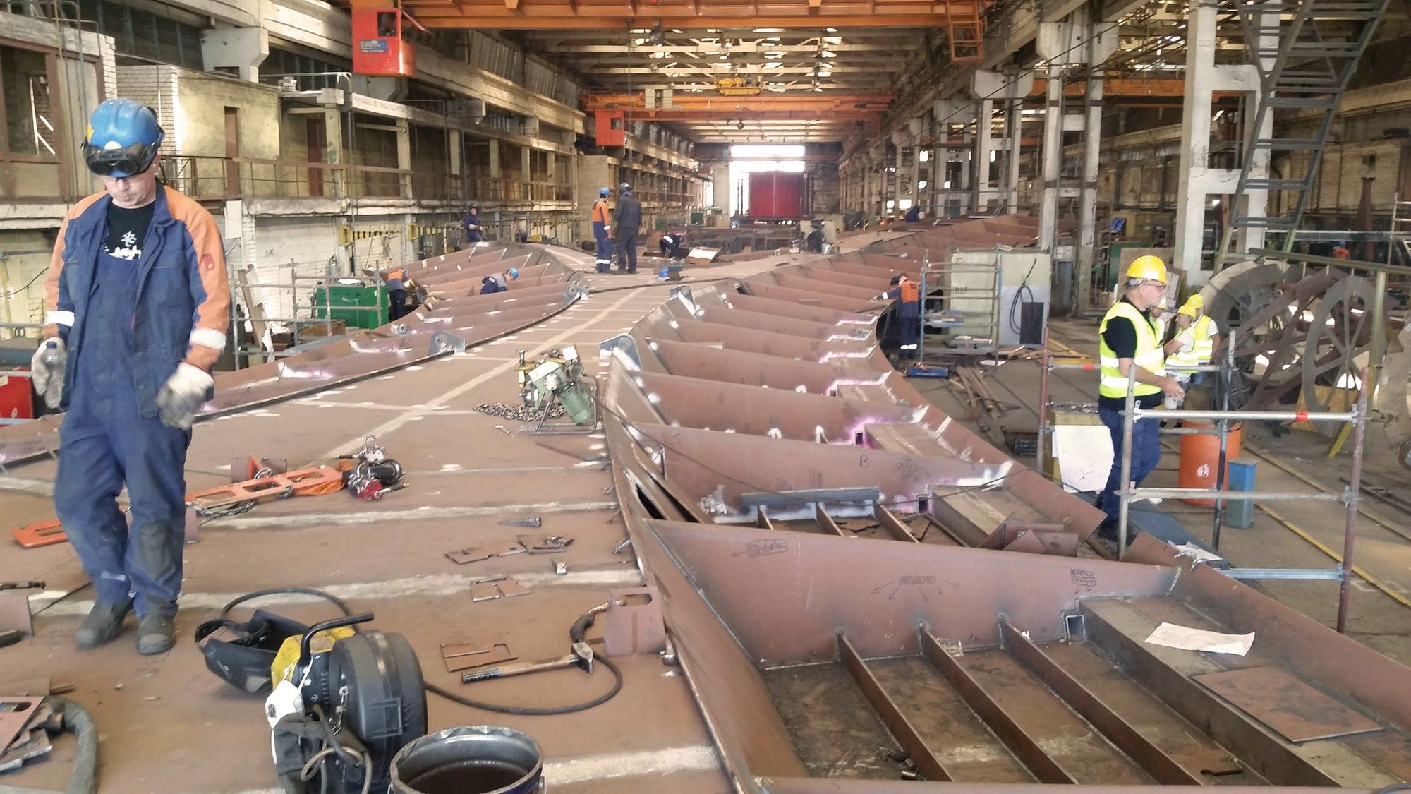 Workers in a large industrial workshop with sections of steel structure