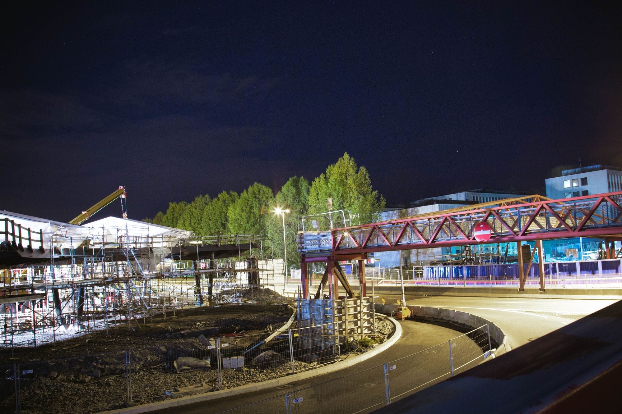 brightly lit bridge at night connecting over a road with surrounding construction equipment