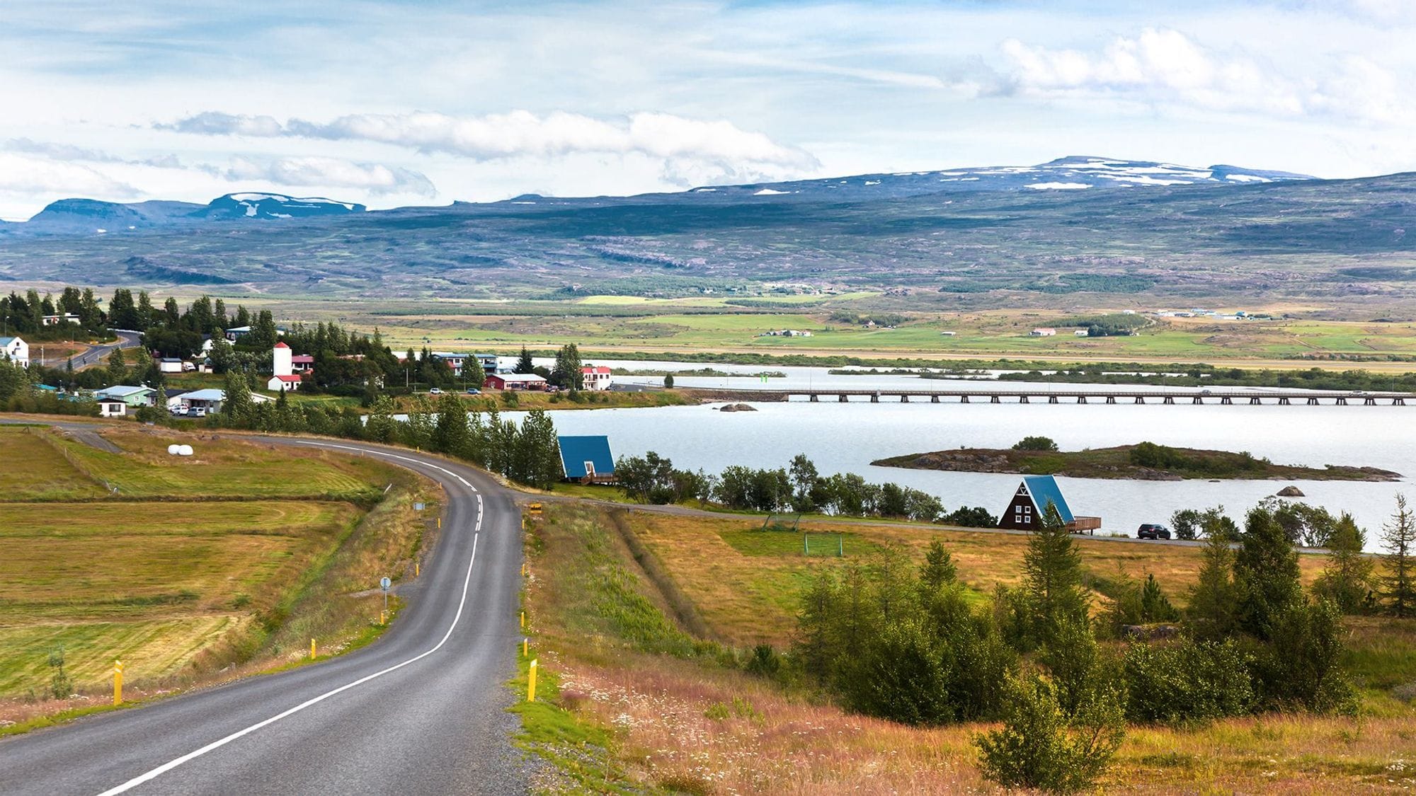 A road leading to a lake and houses scattered across the landscape