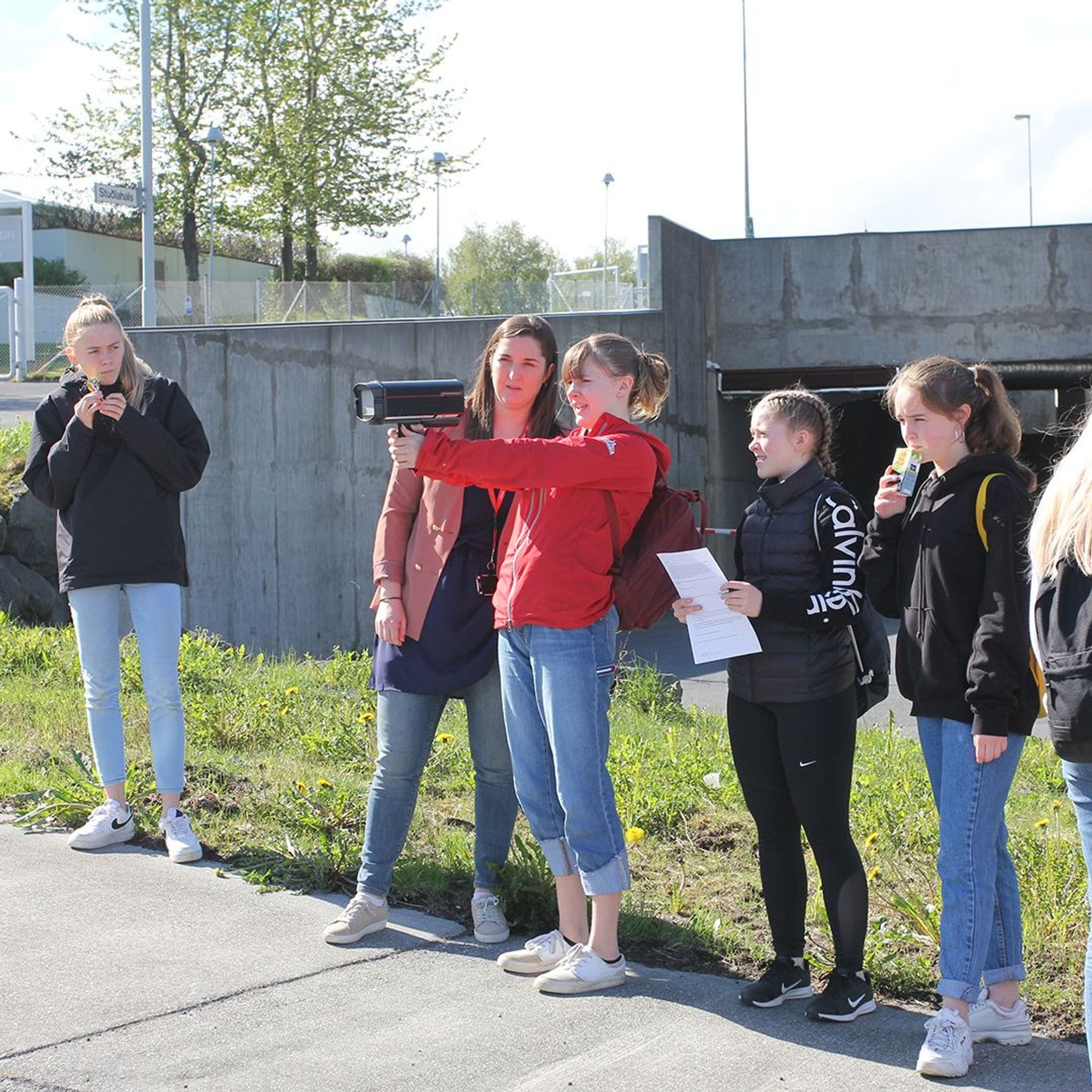 A group of young people outdoors, holding car speed reading machine and and a paper