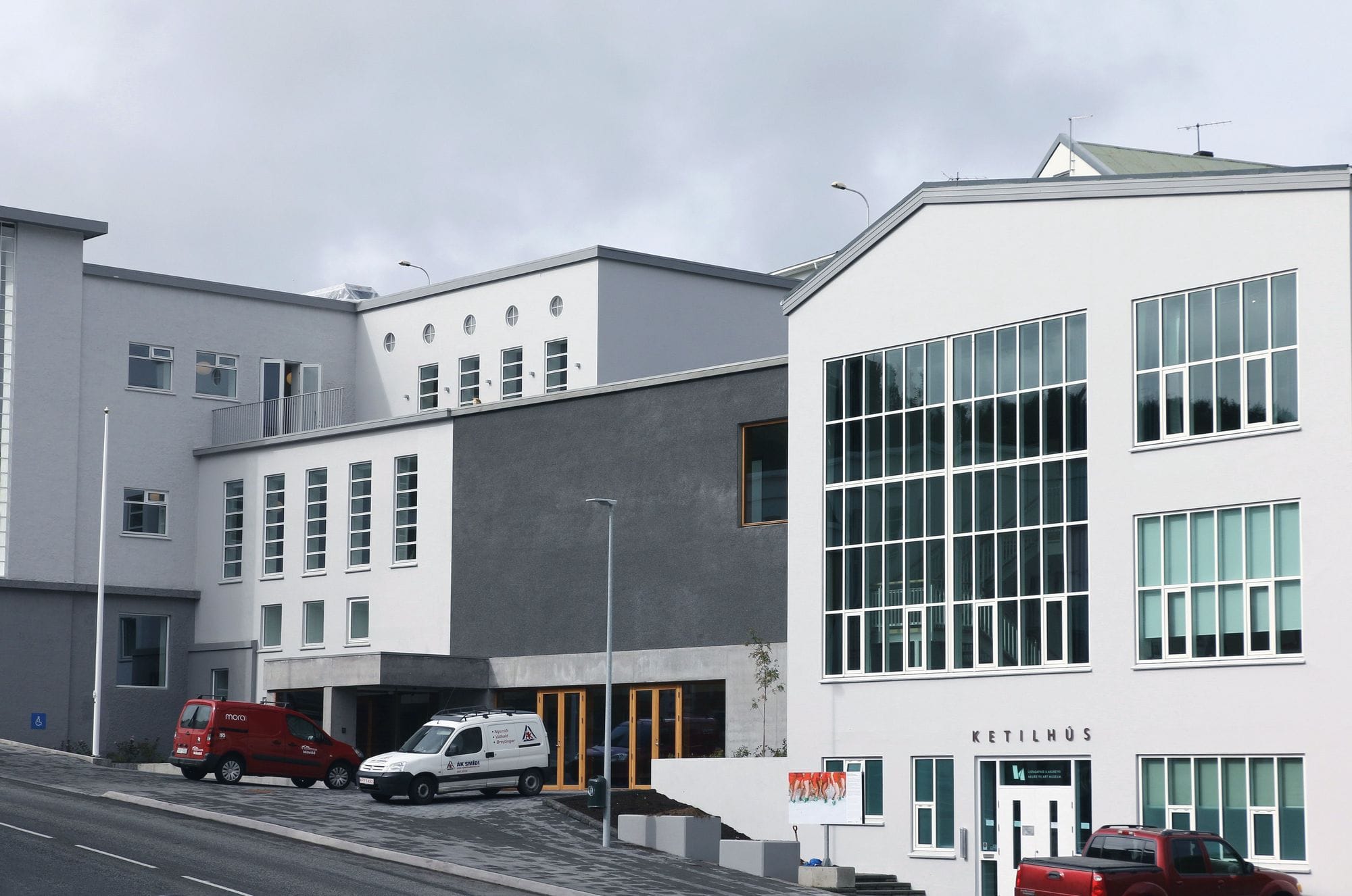 Two cars parked outside white building with several tiny windows