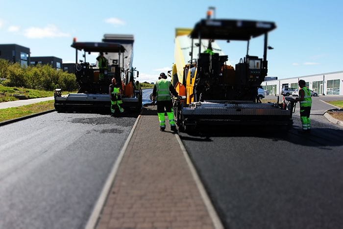 Road construction work in progress where workers are on machinery and road 