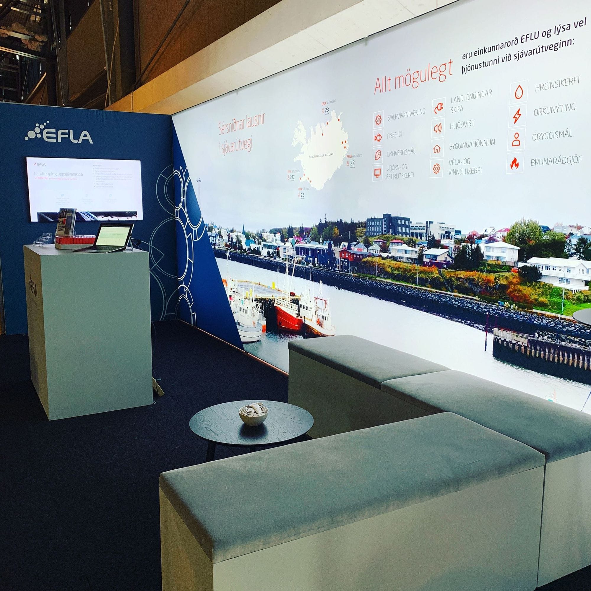 An exhibition stand with a minimalistic design featuring the EFLA company,  sitting area and a monitor