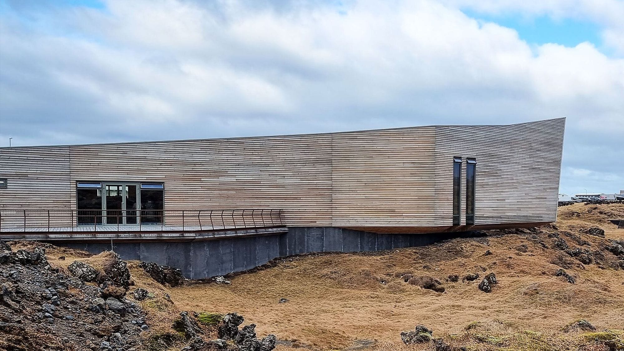 A modern building with unique angled facade, set in rugged landscape with moss covered rocks
