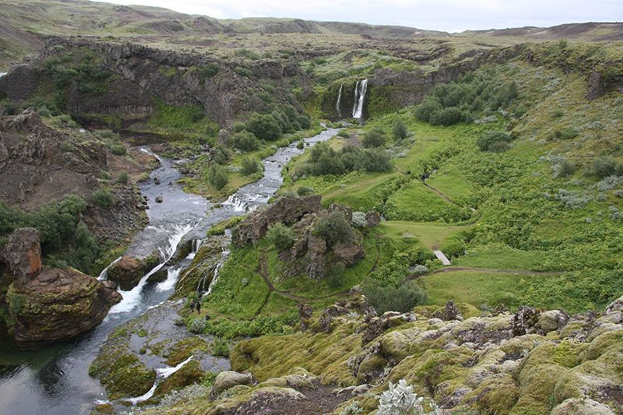 Á sem rennur niður frá fossi í baksýn.