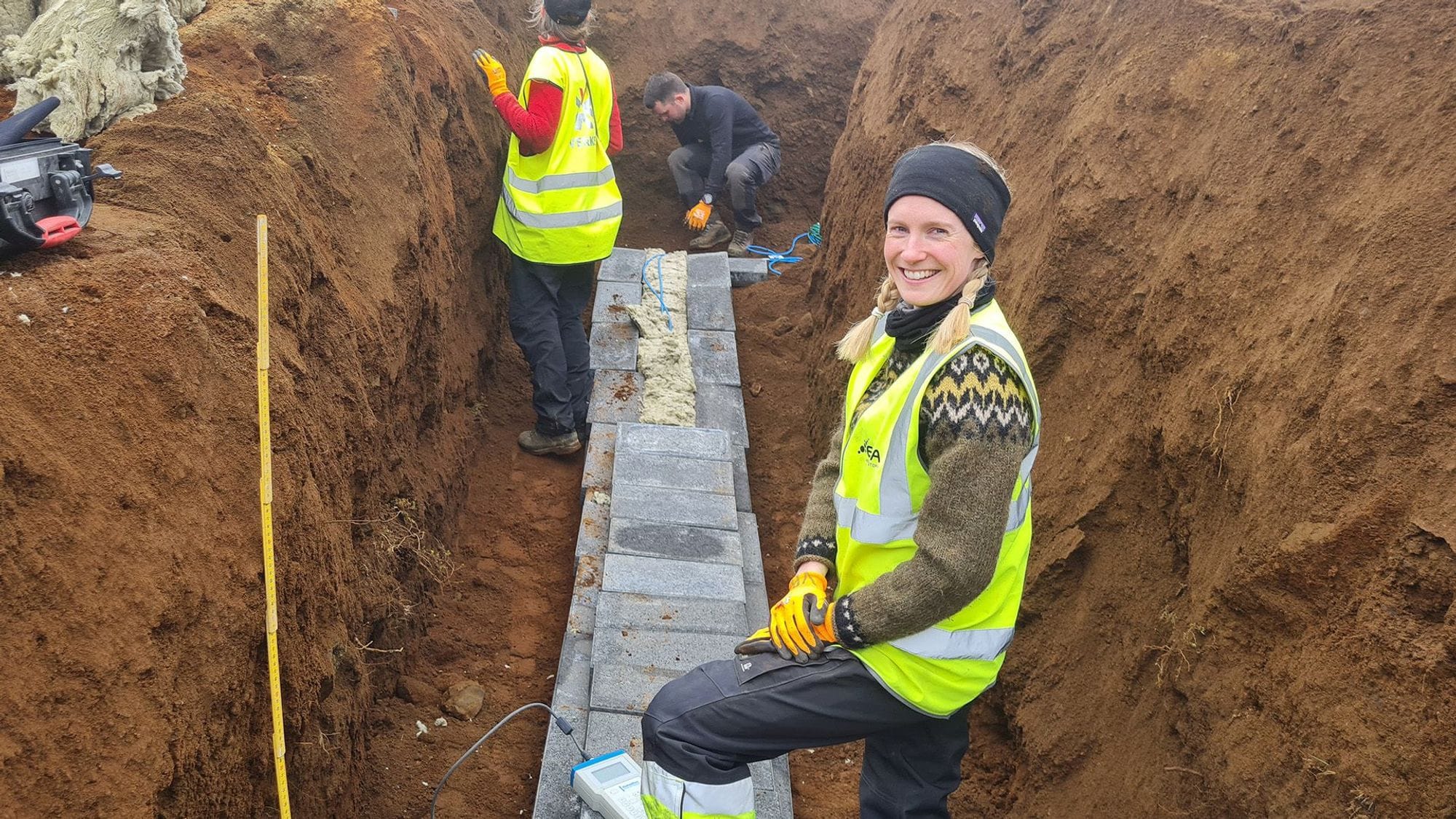 Three individuals wearing high visibility vests working in a deep trench 