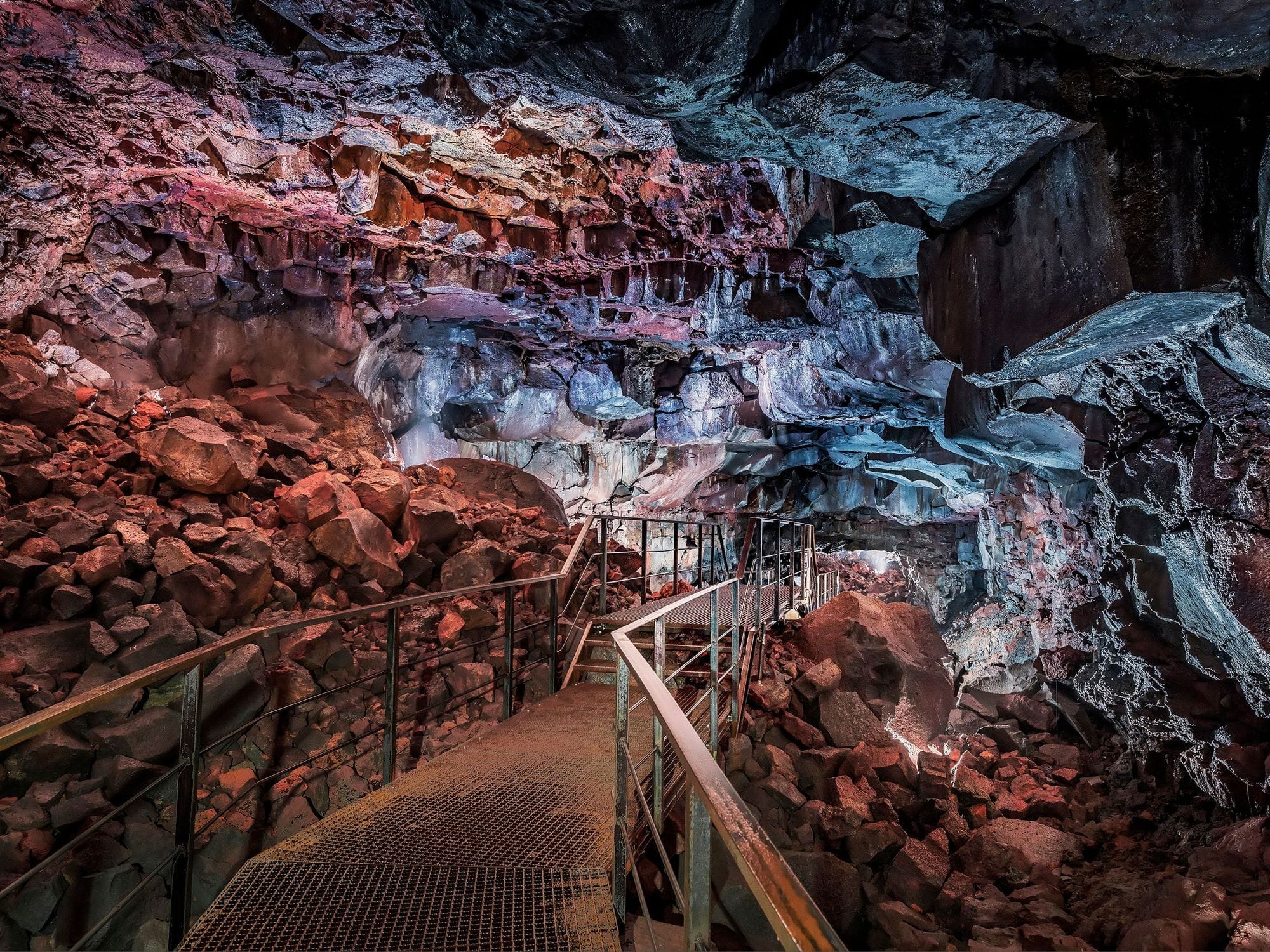 metal stairs leading towards red and blue stone wall in a cave
