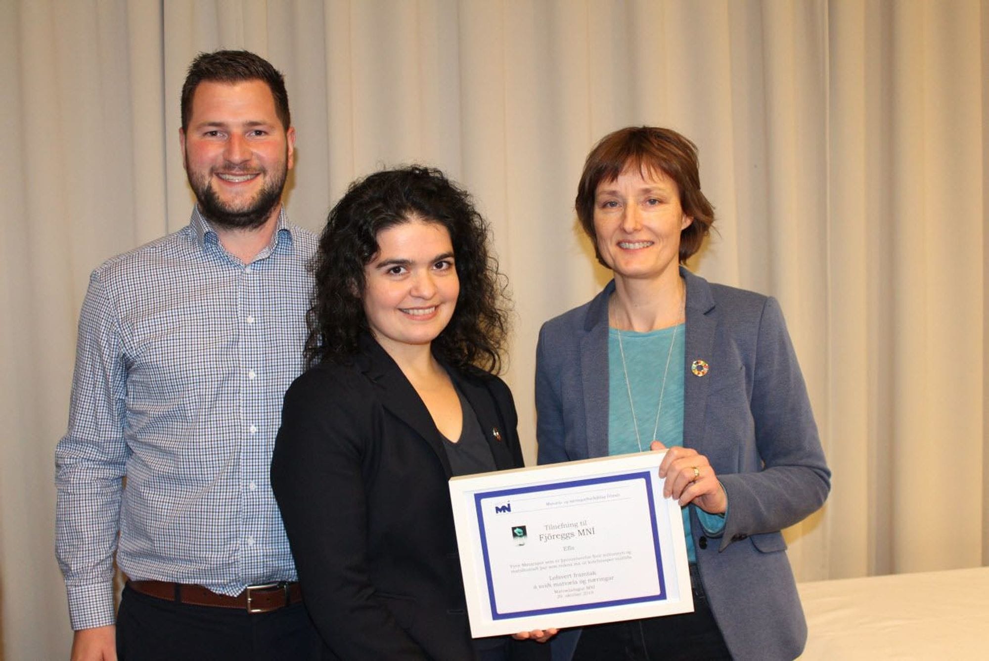 Three individuals posing with smile on their faces, holding white framed certificate