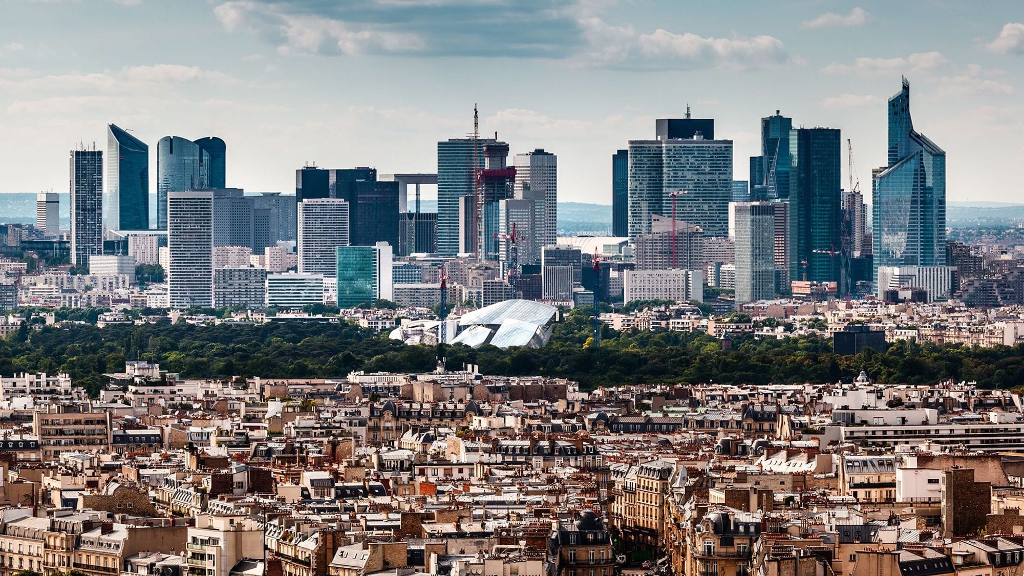 Panoramic view of a densely packed urban area merging into a modern skyline with tall skyscrapers under a cloudy sky