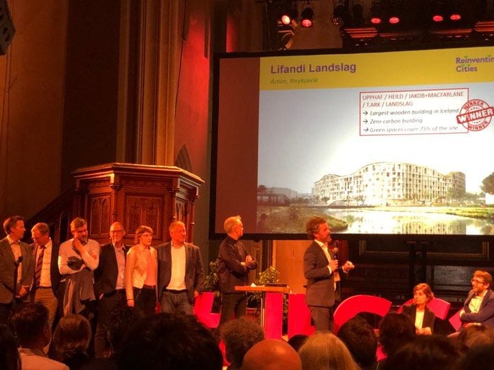 An award ceremony in progress with individuals standing on a stage and a large screen in the background