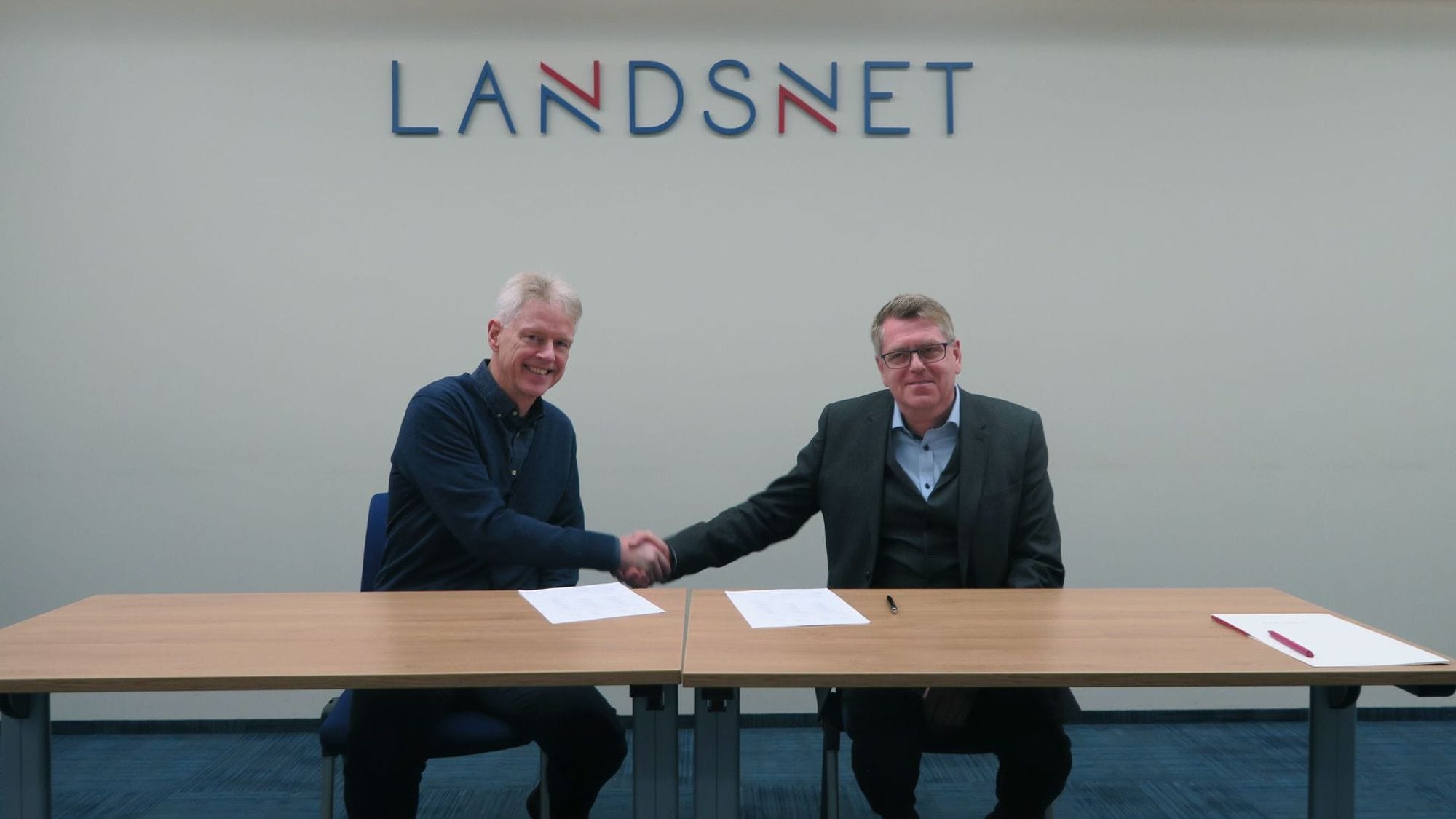 two men shaking hands with documents and pen on a wooden table