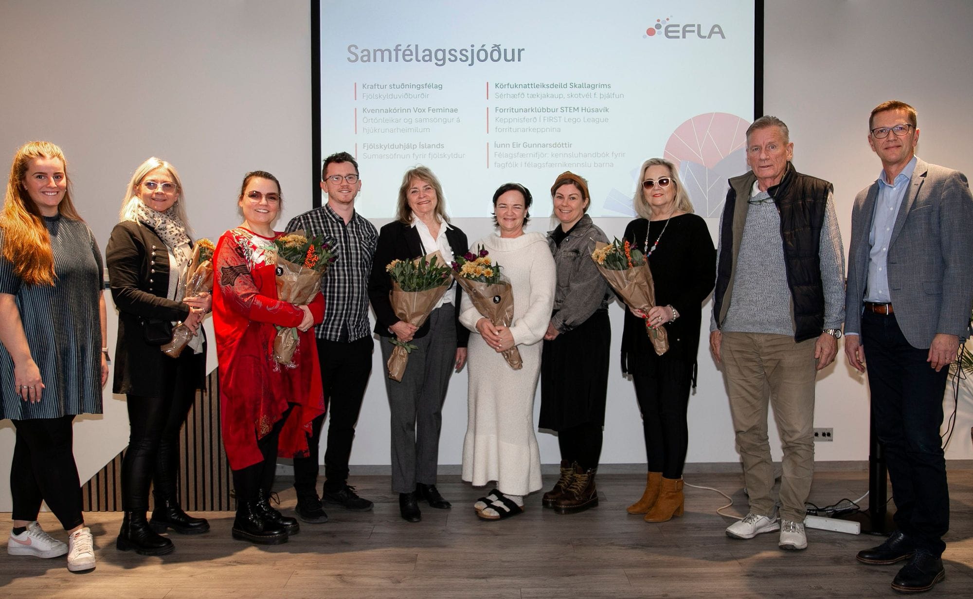 A large group of people holding bouquet of flower with a big screen in the background