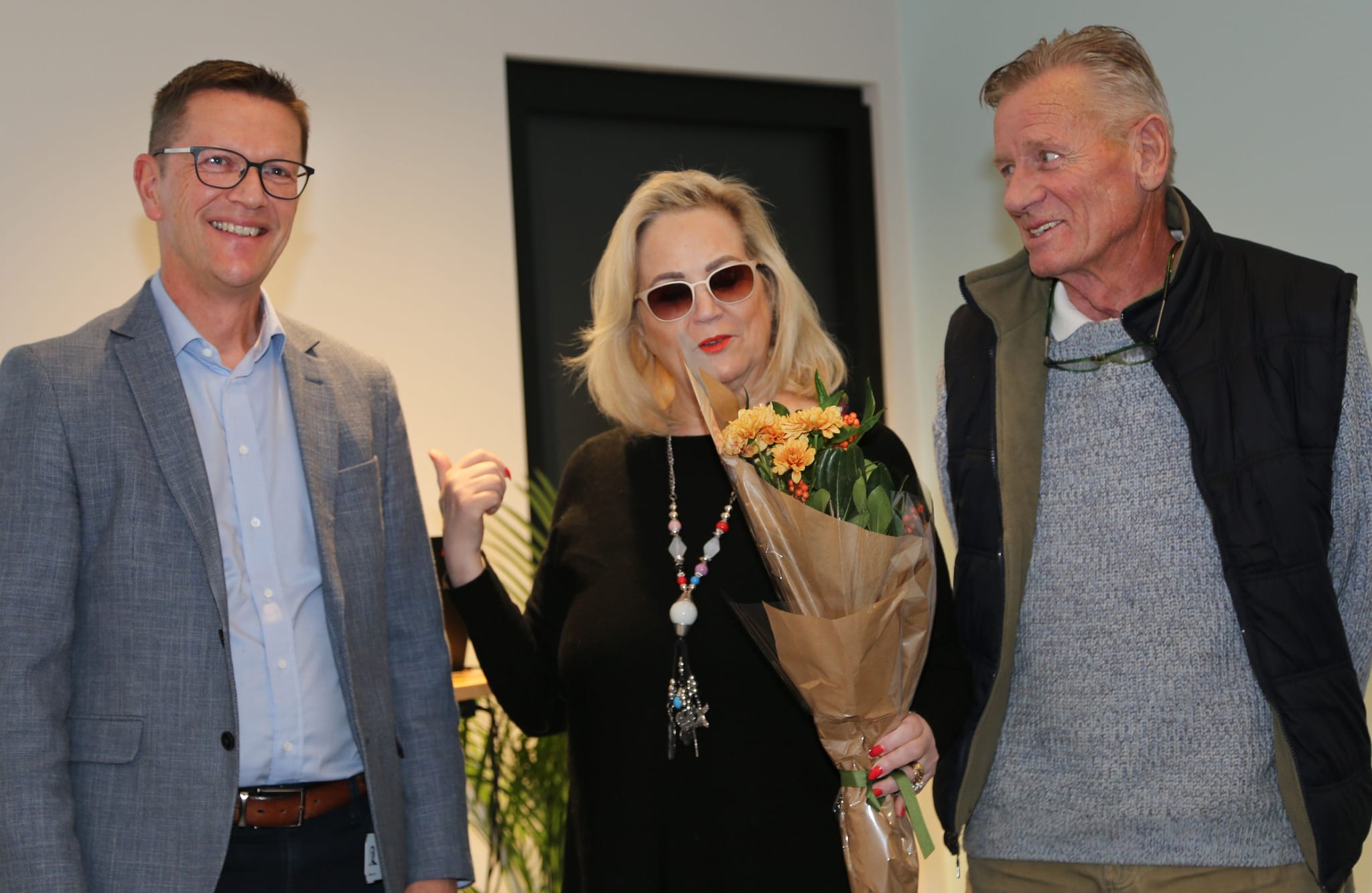 Three individuals standing in front of a presentation screen, with one person holding a bouquet of flowers