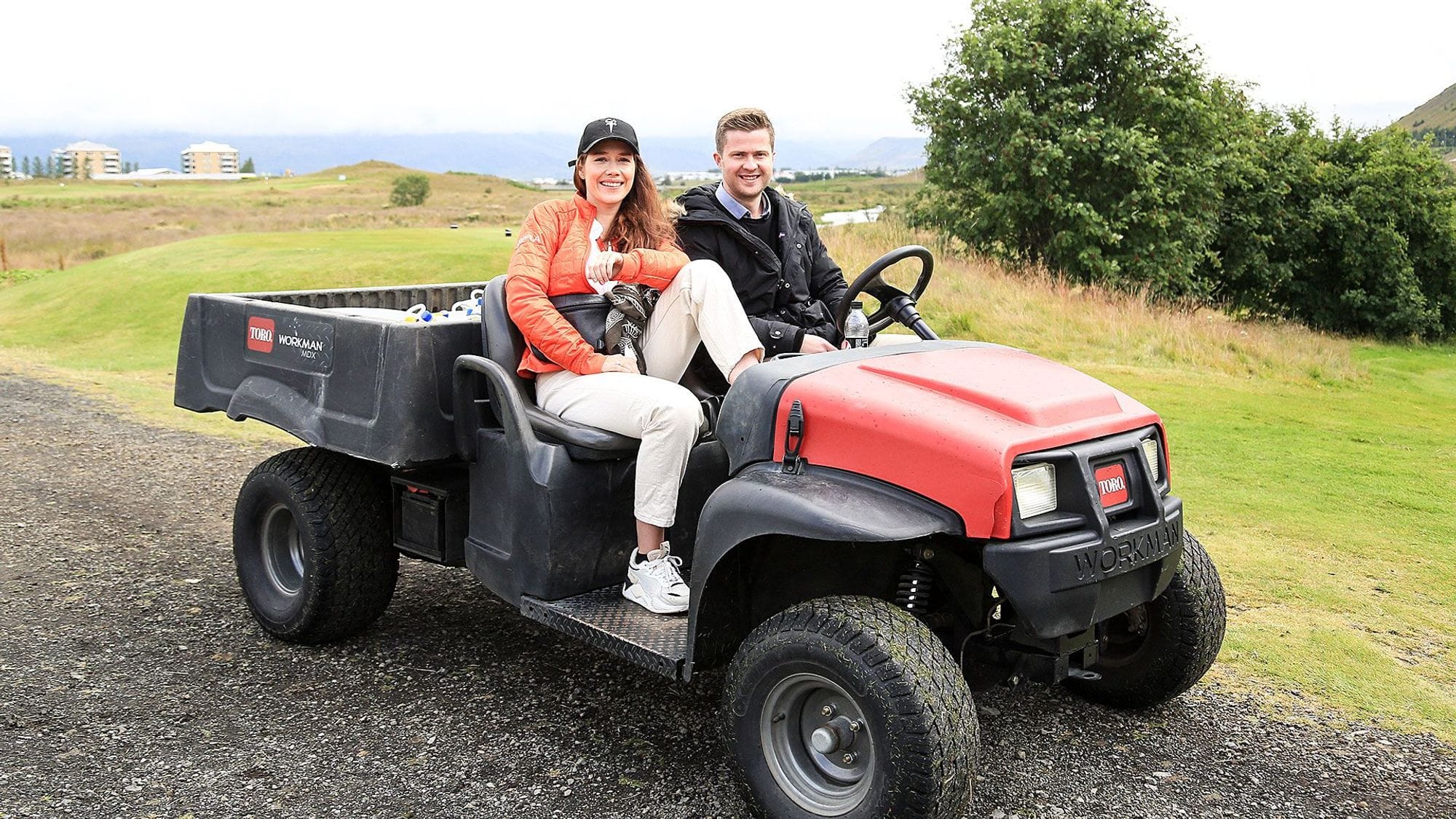 Two individuals seated on a red and black golf utility vehicle