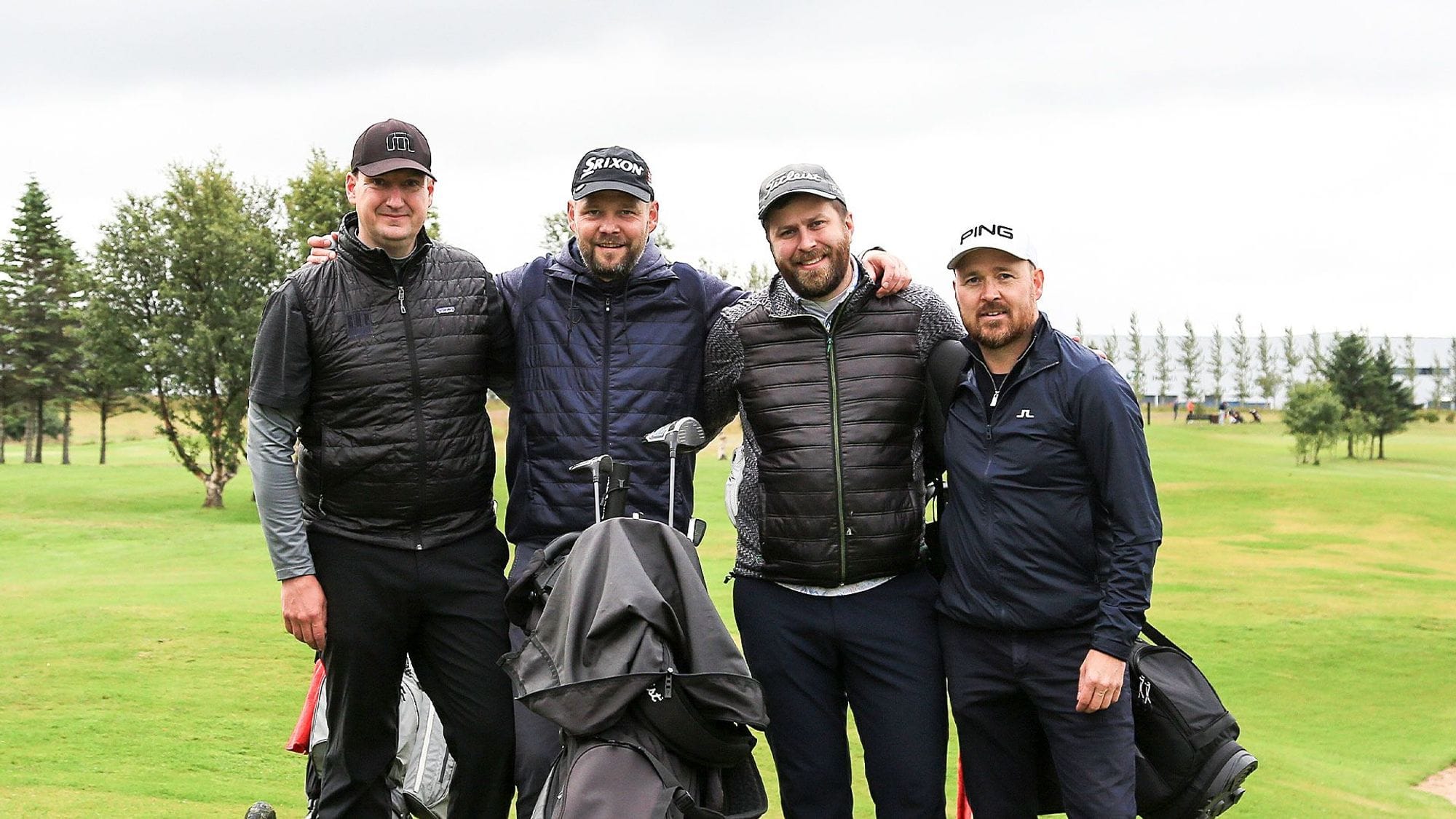 Four men standing with a golf bag on a course with trees 