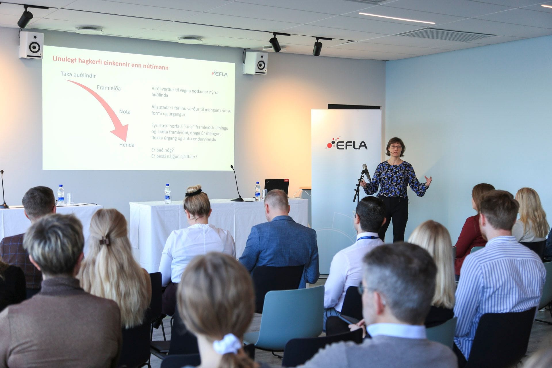 An audience listening to a speaker at a conference or presentation with the "EFLA" banner and big screen in the background