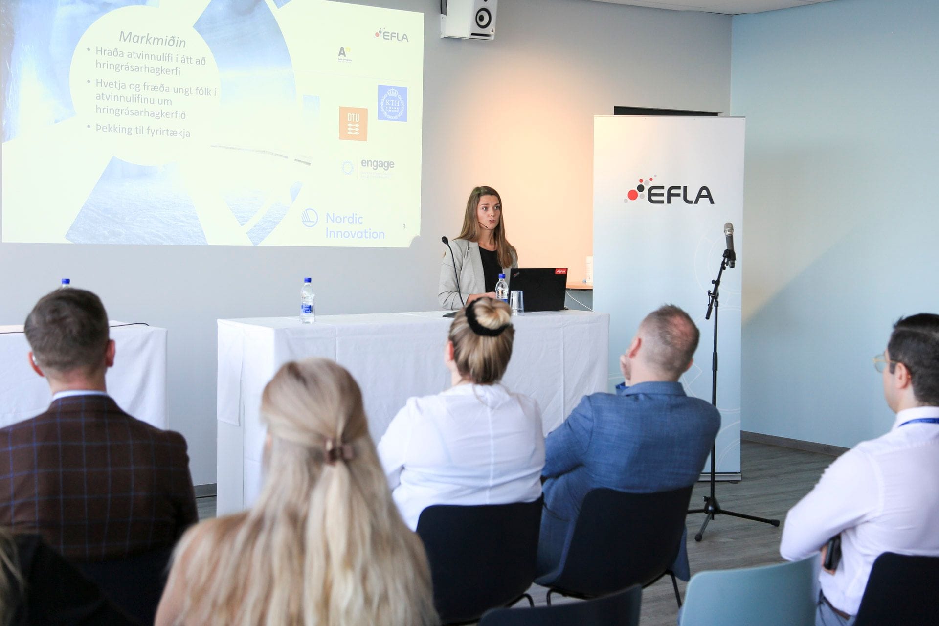 An audience listening to a speaker seated with a laptop at a conference or presentation with the "EFLA" banner close to her