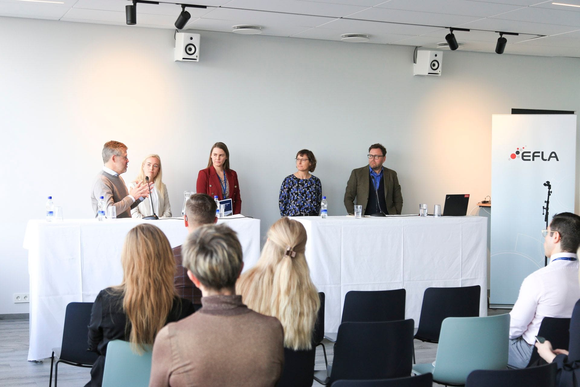 The photo shows a discussion between  five individuals in front of a room of attentive listeners