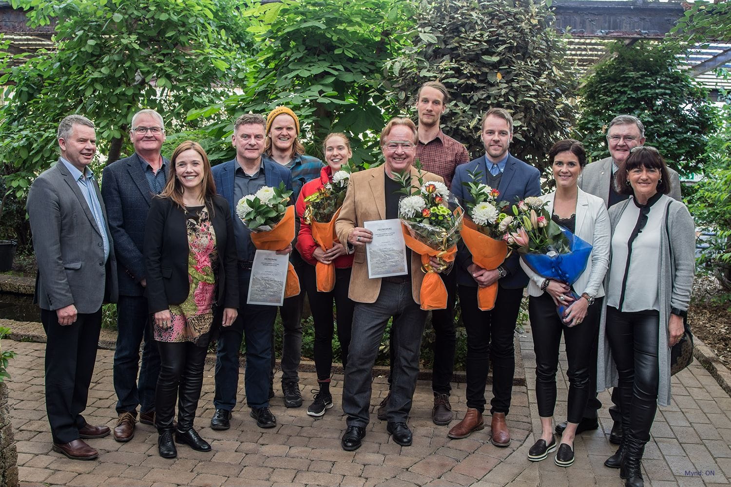 a group of people smiling and holding certificates and bouquets