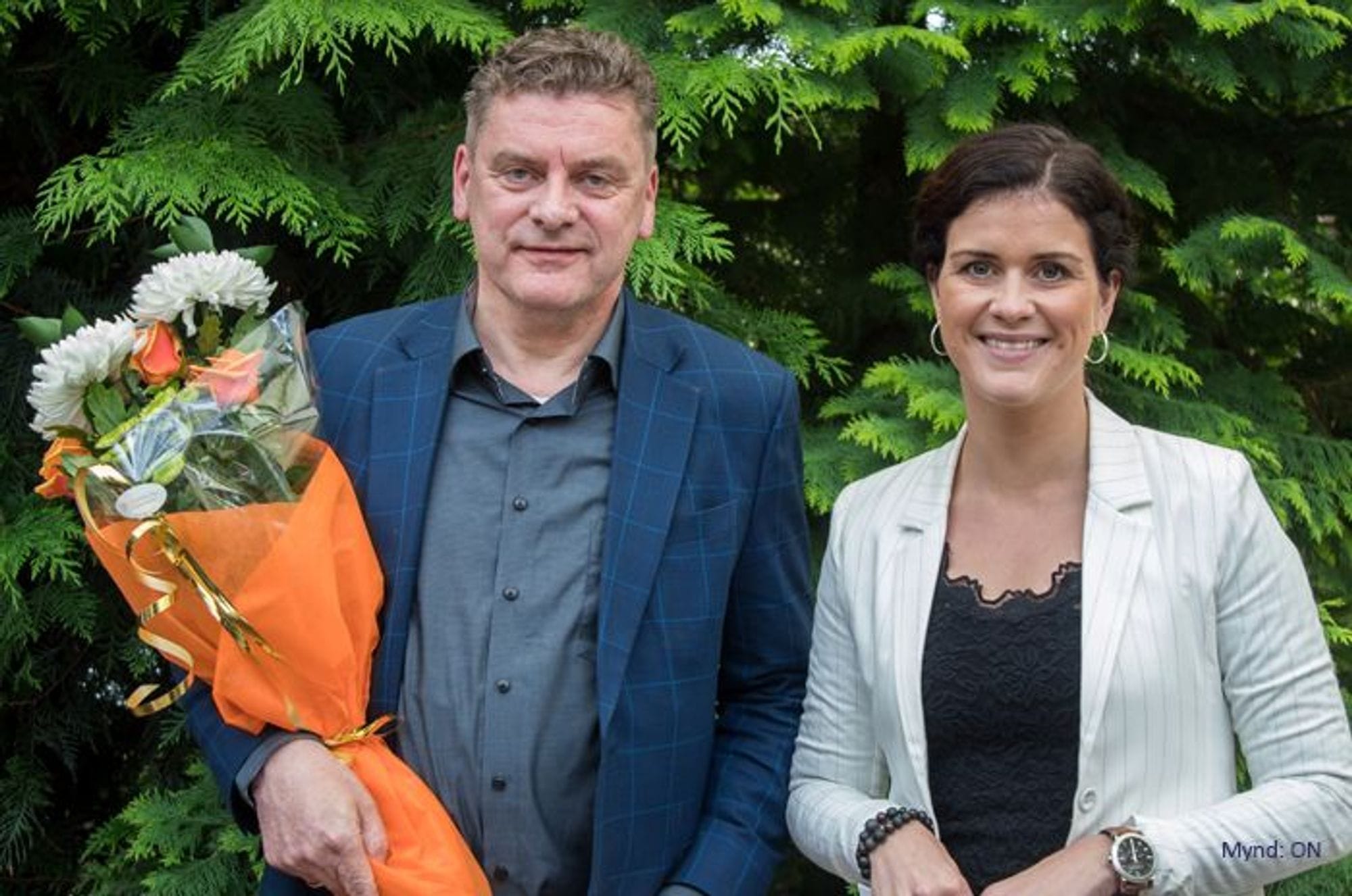 A man holding bouquet standing next to a woman wearing white blazer