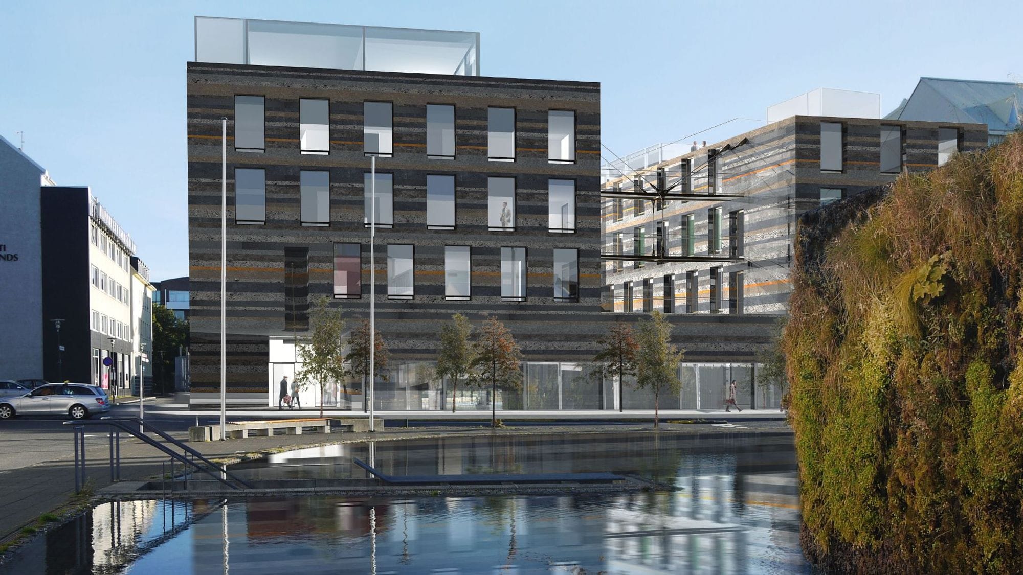 A modern multi-story building with large windows and dark cladding, reflected in a lake in front of it
