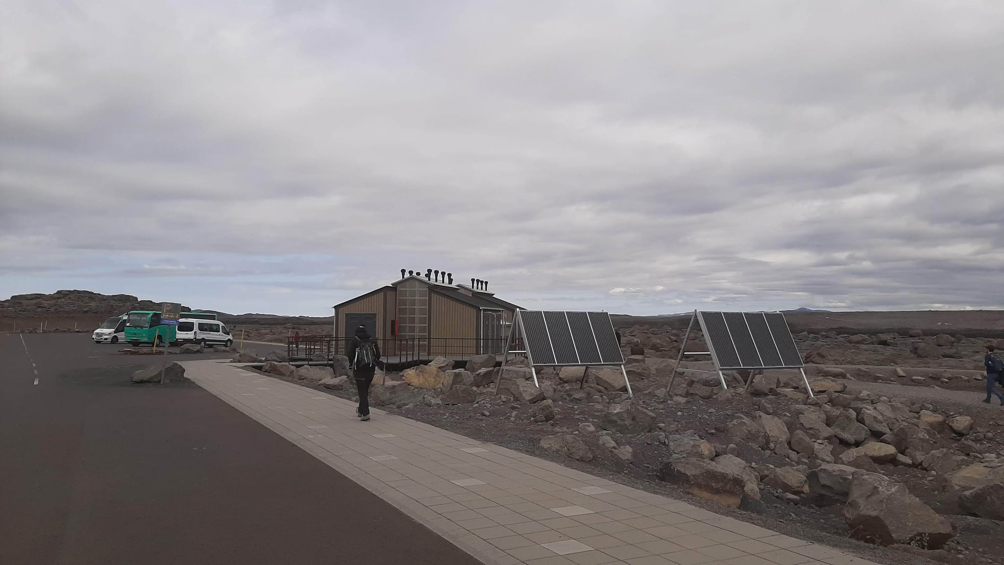 A person walking towards small cabin like structure with dark roof next to two solar cells