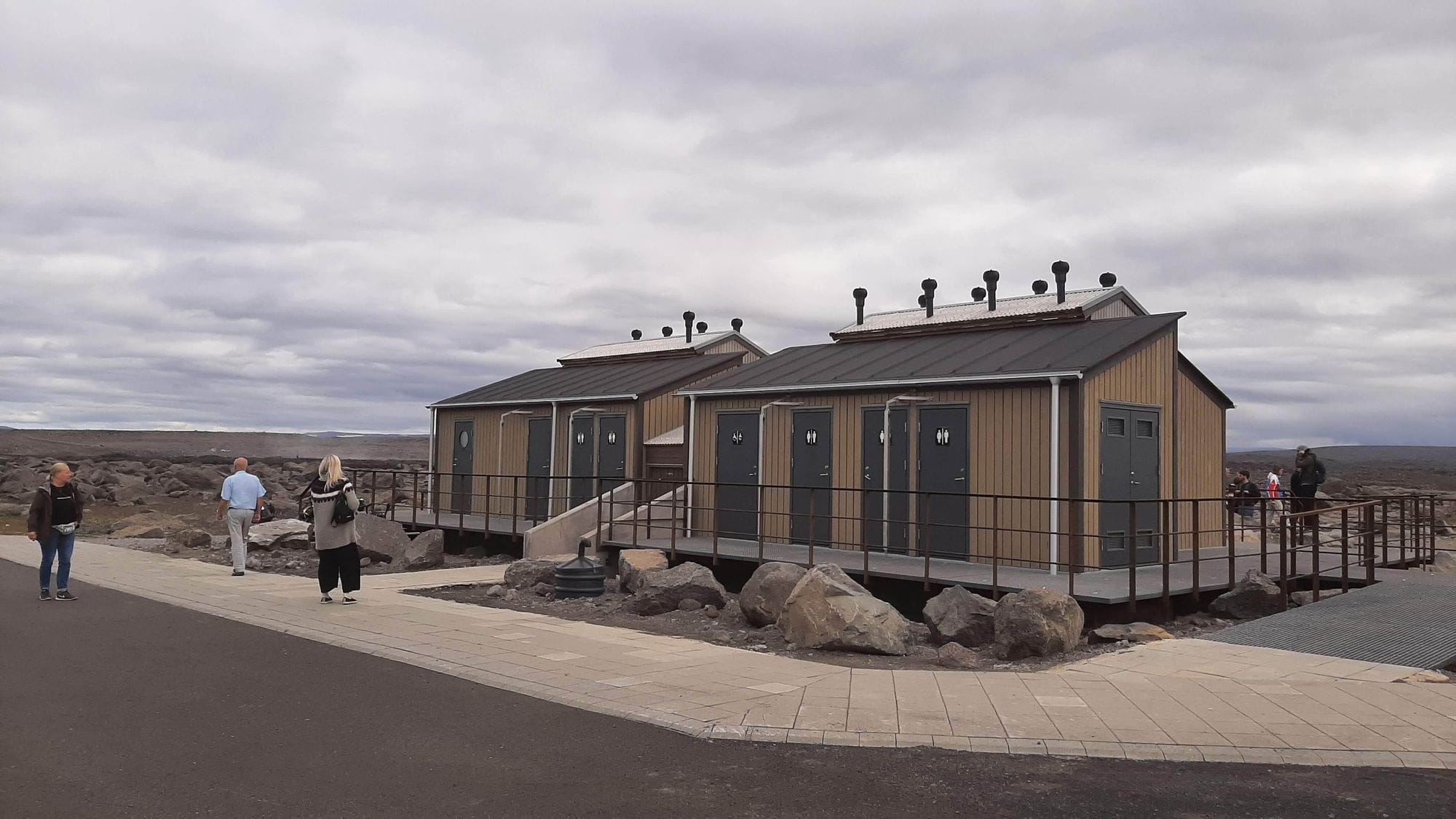 People walking towards small cabin like structure with dark roof 
