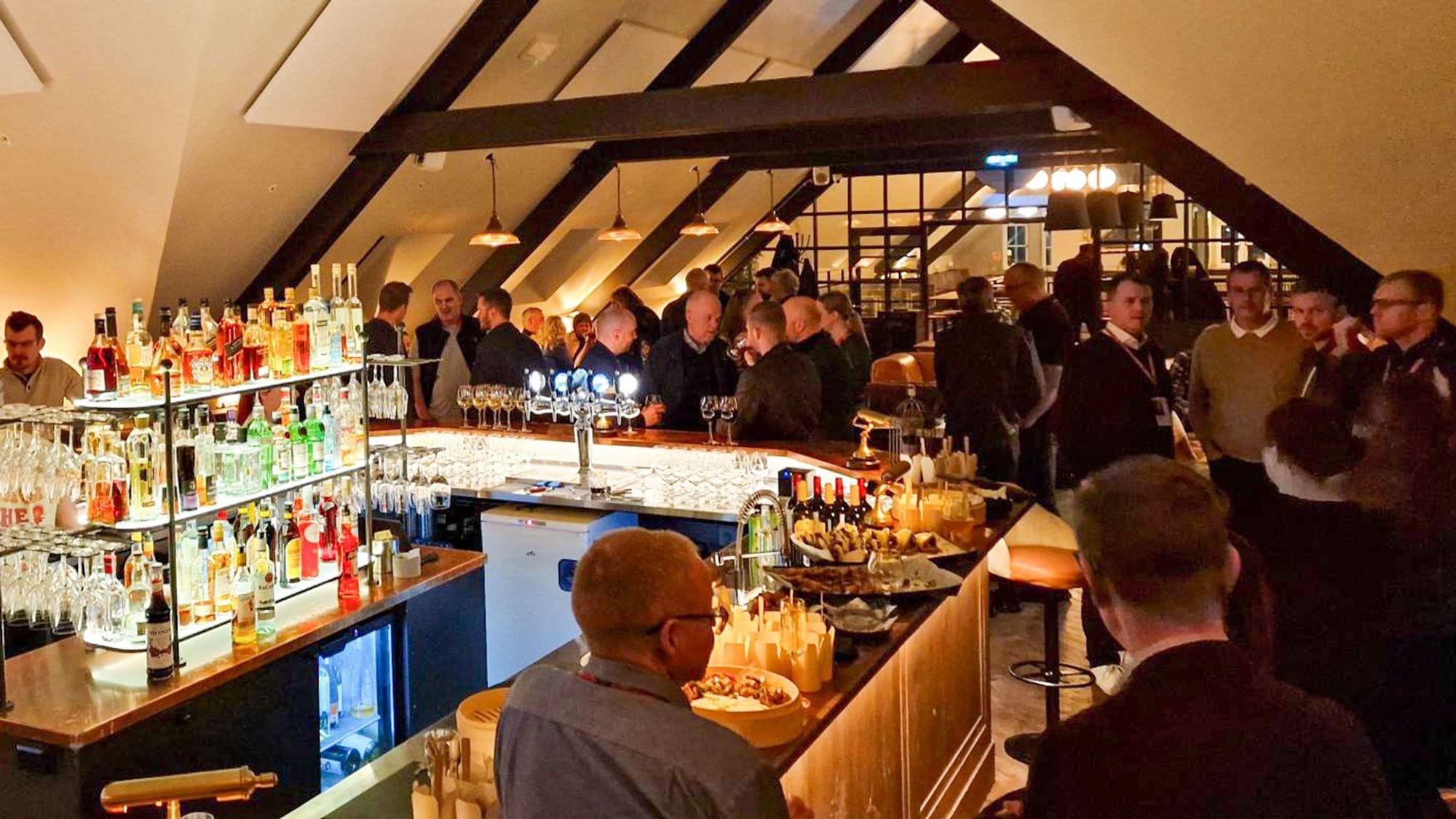 Fólk í samkomu við bar undir risi.