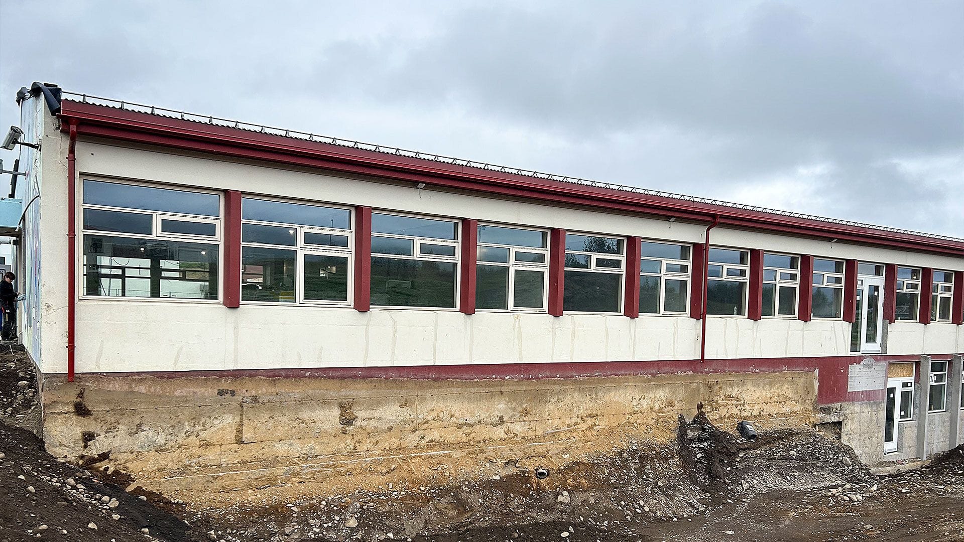 A single-story building with a long row of windows, situated on an exposed soil and rock foundation