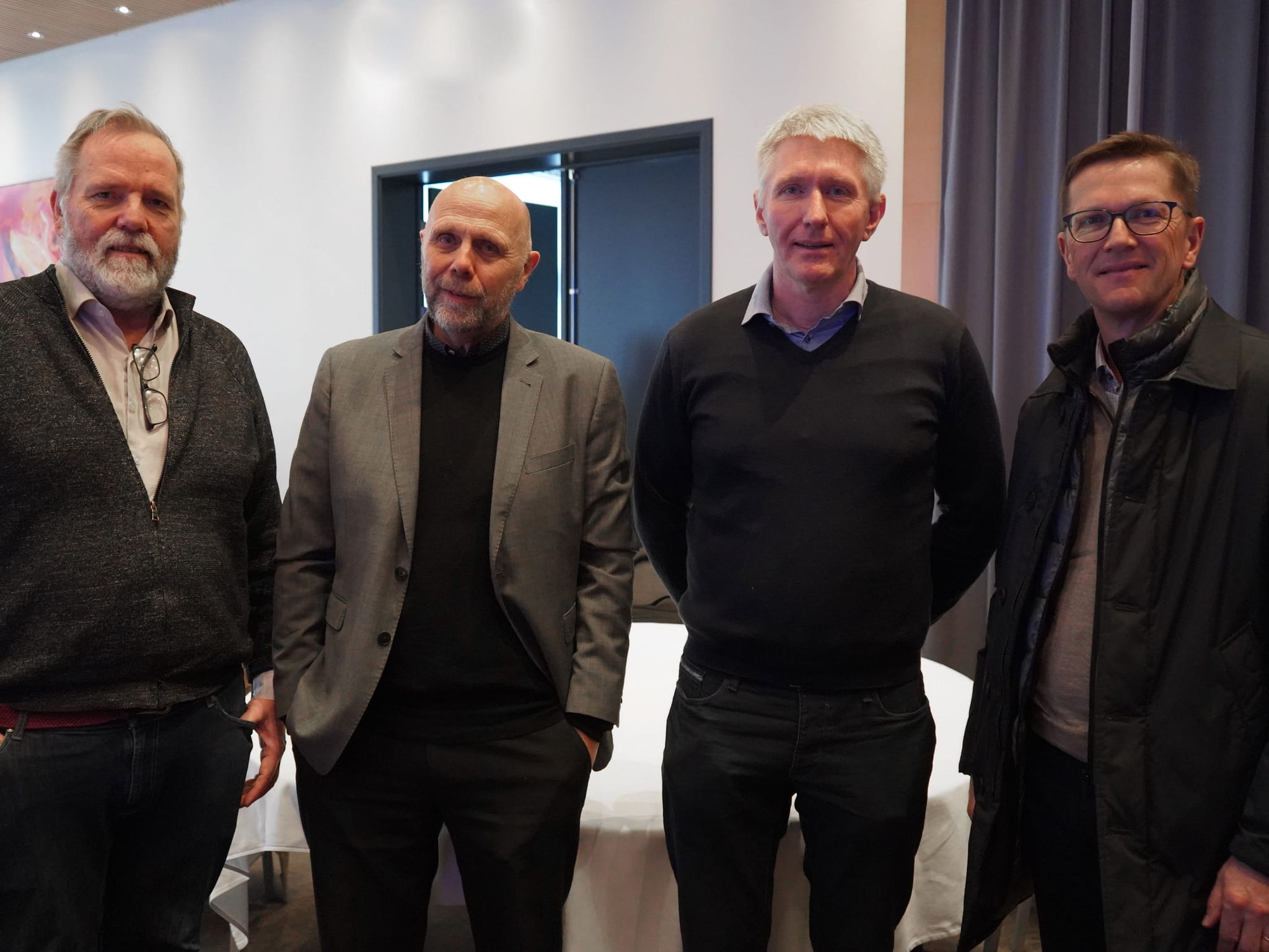Four men standing together for a photo, dressed in business casual attire