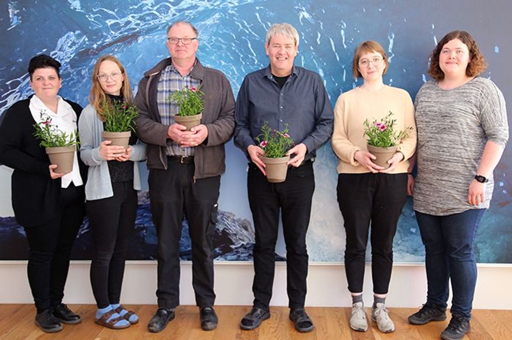 A group of six individuals standing and holding potted plats