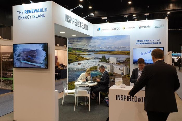 people sitting and standing in a trade show booth with banner reading "THE RENEWABLE ENERGY ISLAND"