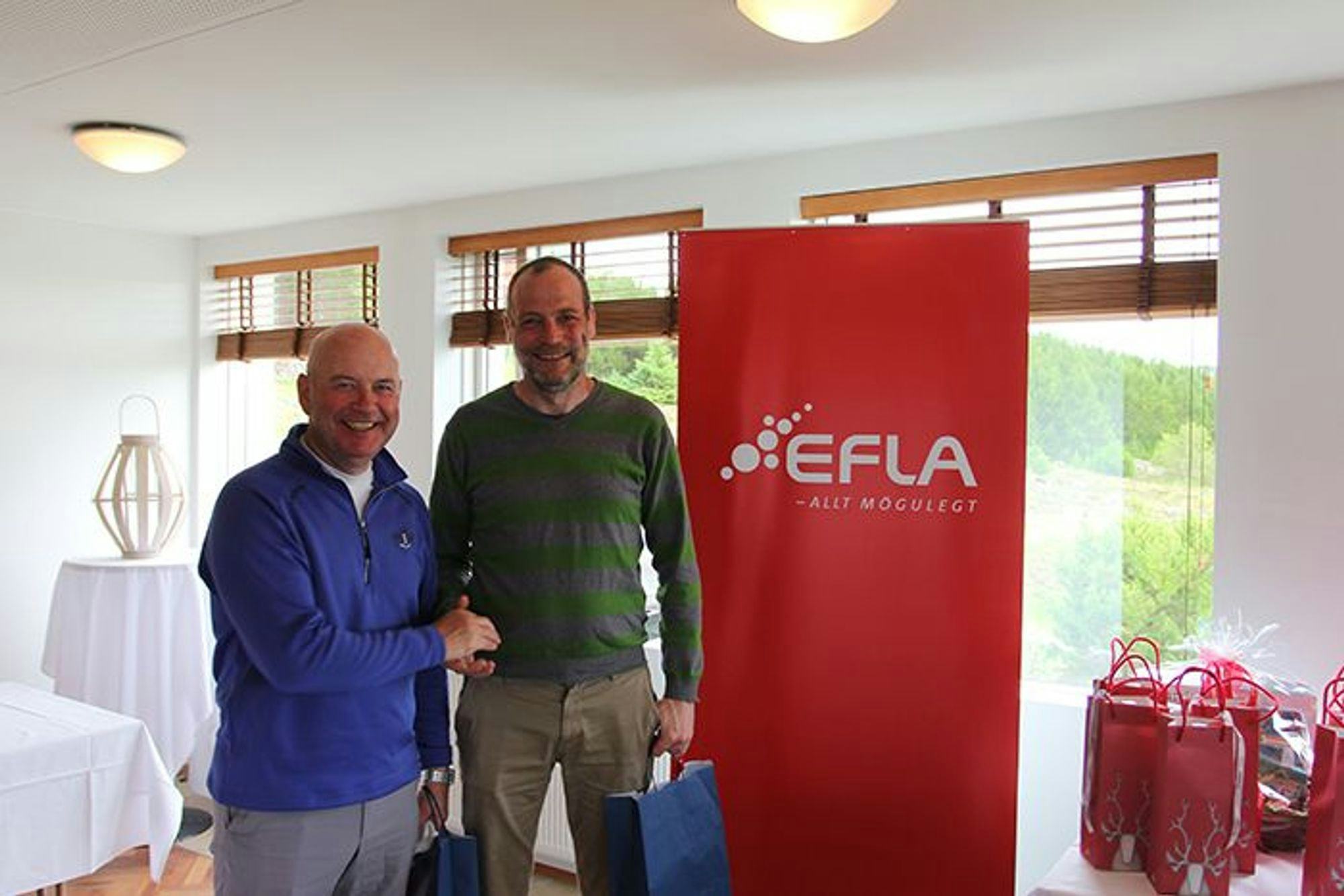 Two men standing in front of a red EFLA promotional banner