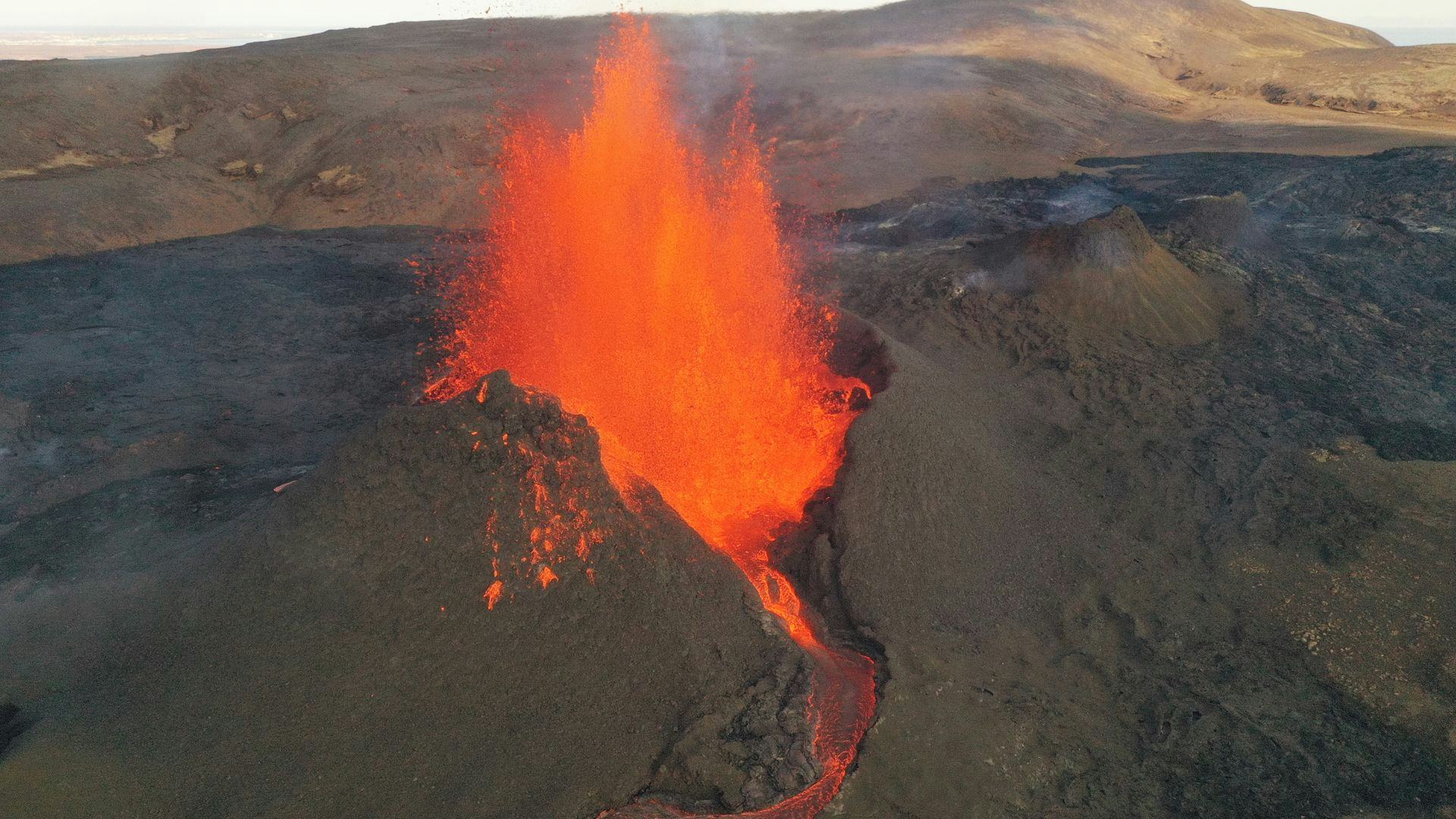 A volcanic eruption with bright orange lava spewing from a fissure on a ruged landscape