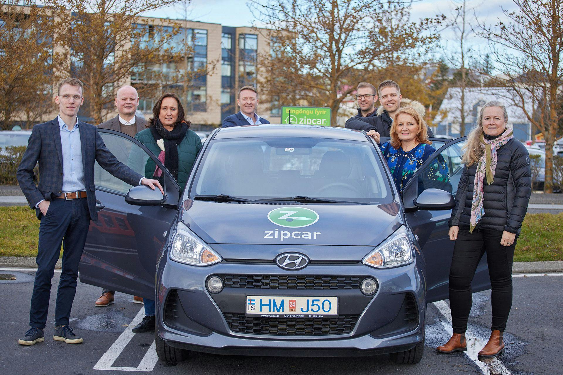 A group of people posing with a Hyundai Zipcar in a parking lot 