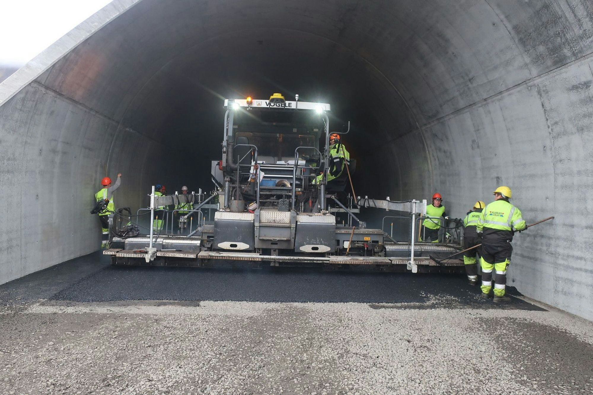 Construction workers and heavy machinery paving the interior of a tunnel