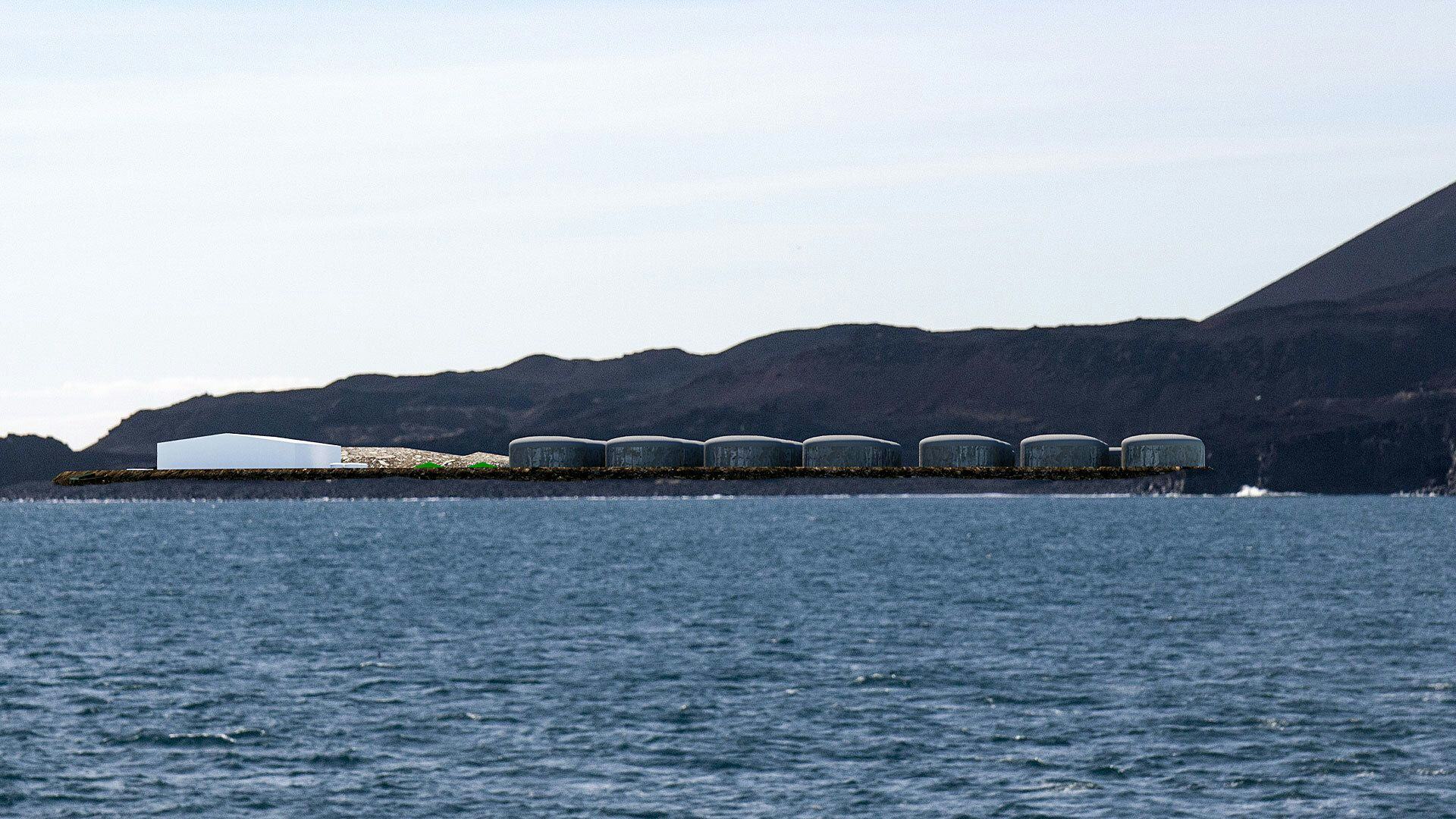 A series of rounded barrel shaped structures on a coastline set against mountain backdrop