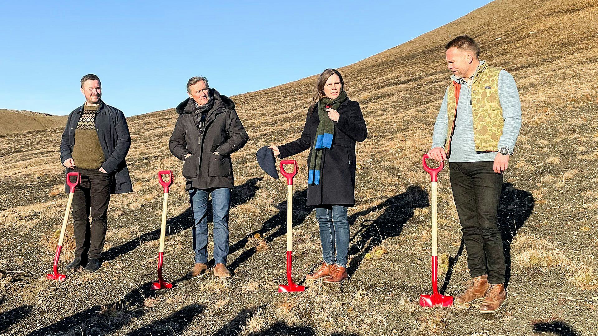 Four individuals dressed in warm clothing, standing outdoors with shovels in their hands