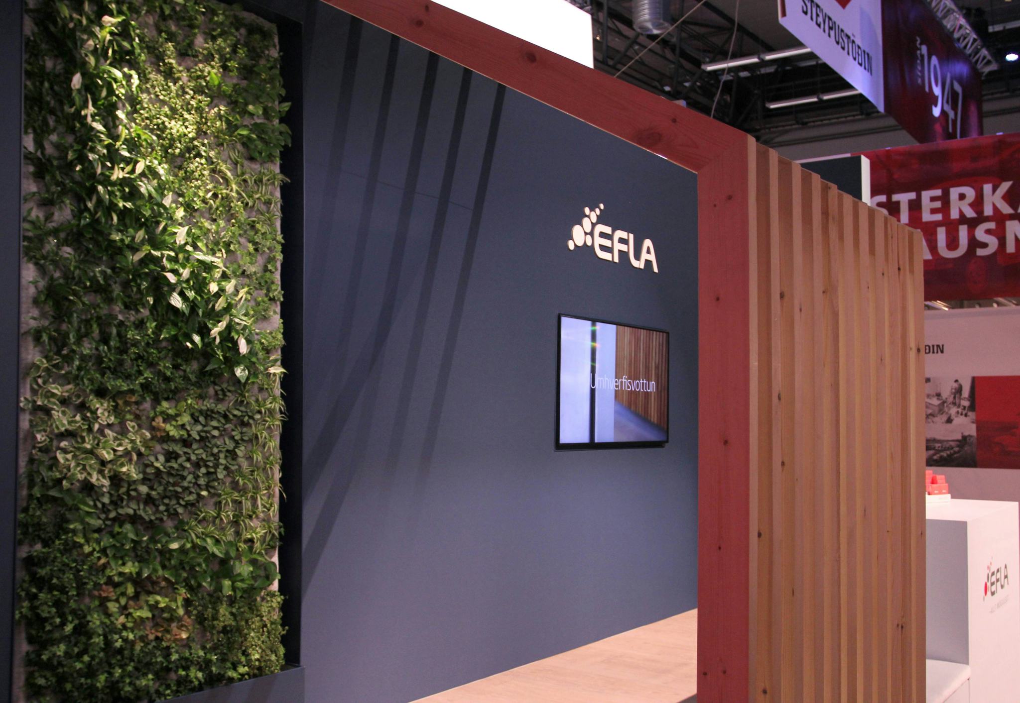 An indoor exhibition stand with a green wall on the left and a dark blue partition with the logo of EFLA. To the right, there is a wooden structure wall.