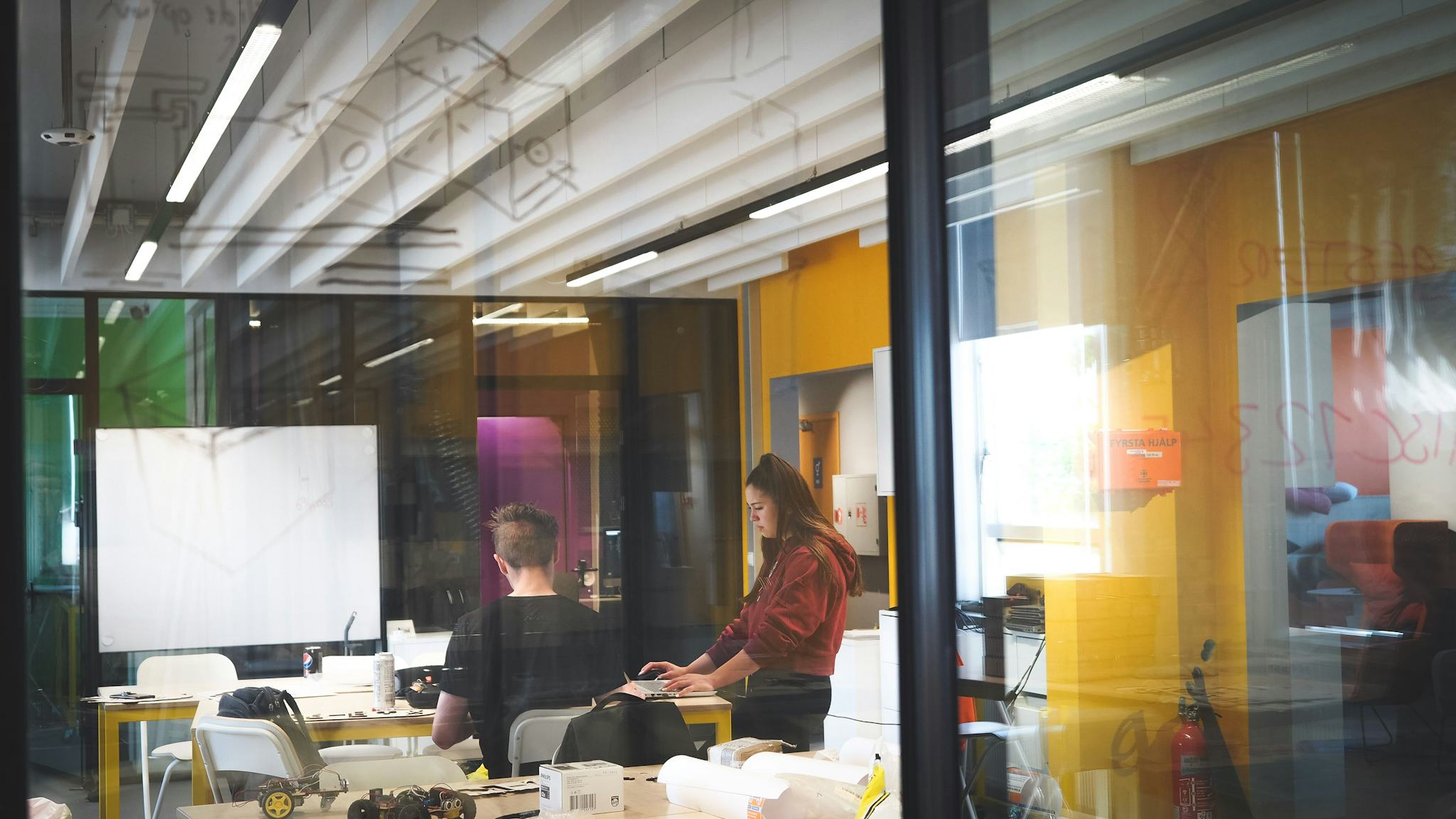 Two people working at desks in a brightly lit modern office space with vibrant yellow walls