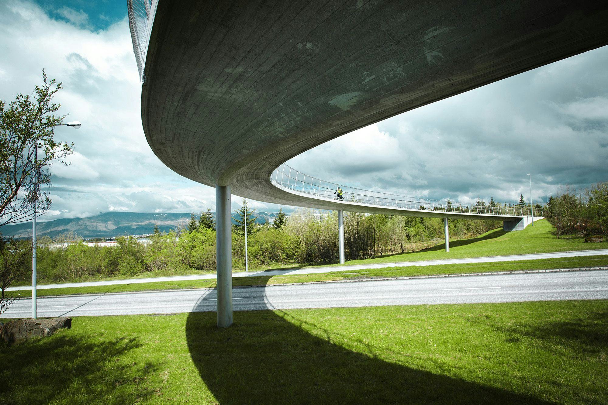 An elegant, curving structure of a pedestrian bridge with a smooth underbelly, under cloudy sky