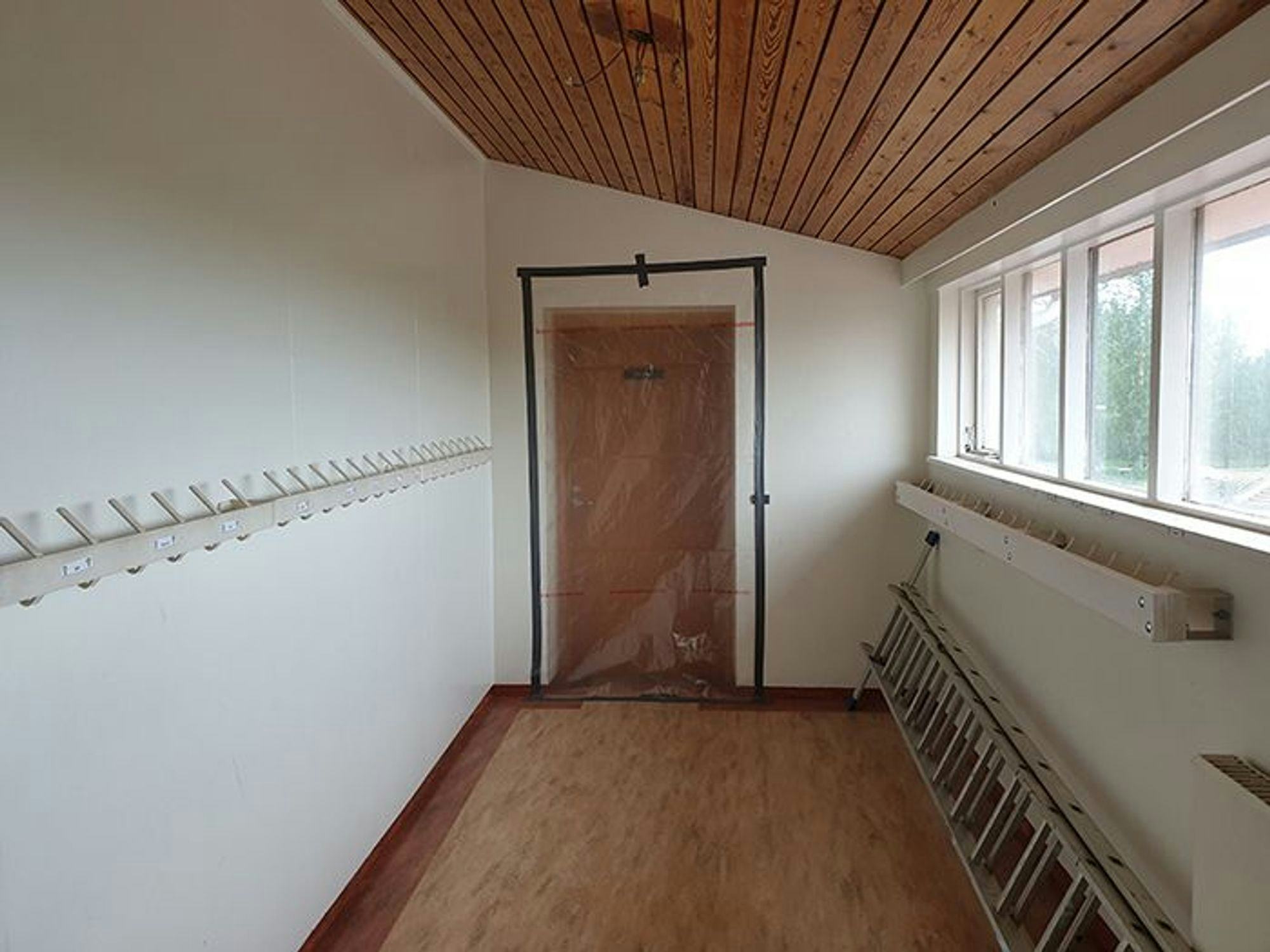 A small empty with wooden floor, ceiling and door and small windows