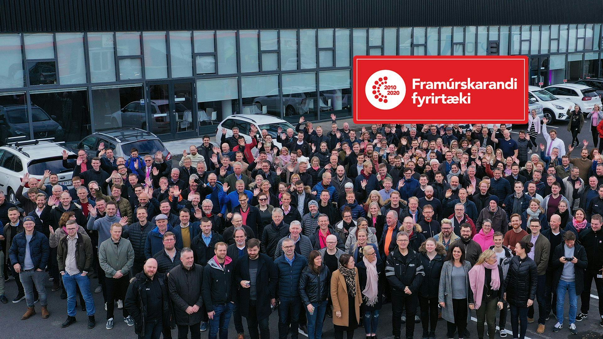 A group of people gathered in front of a modern building with some Icelandic text "Framurskarandi fyrirtæki"