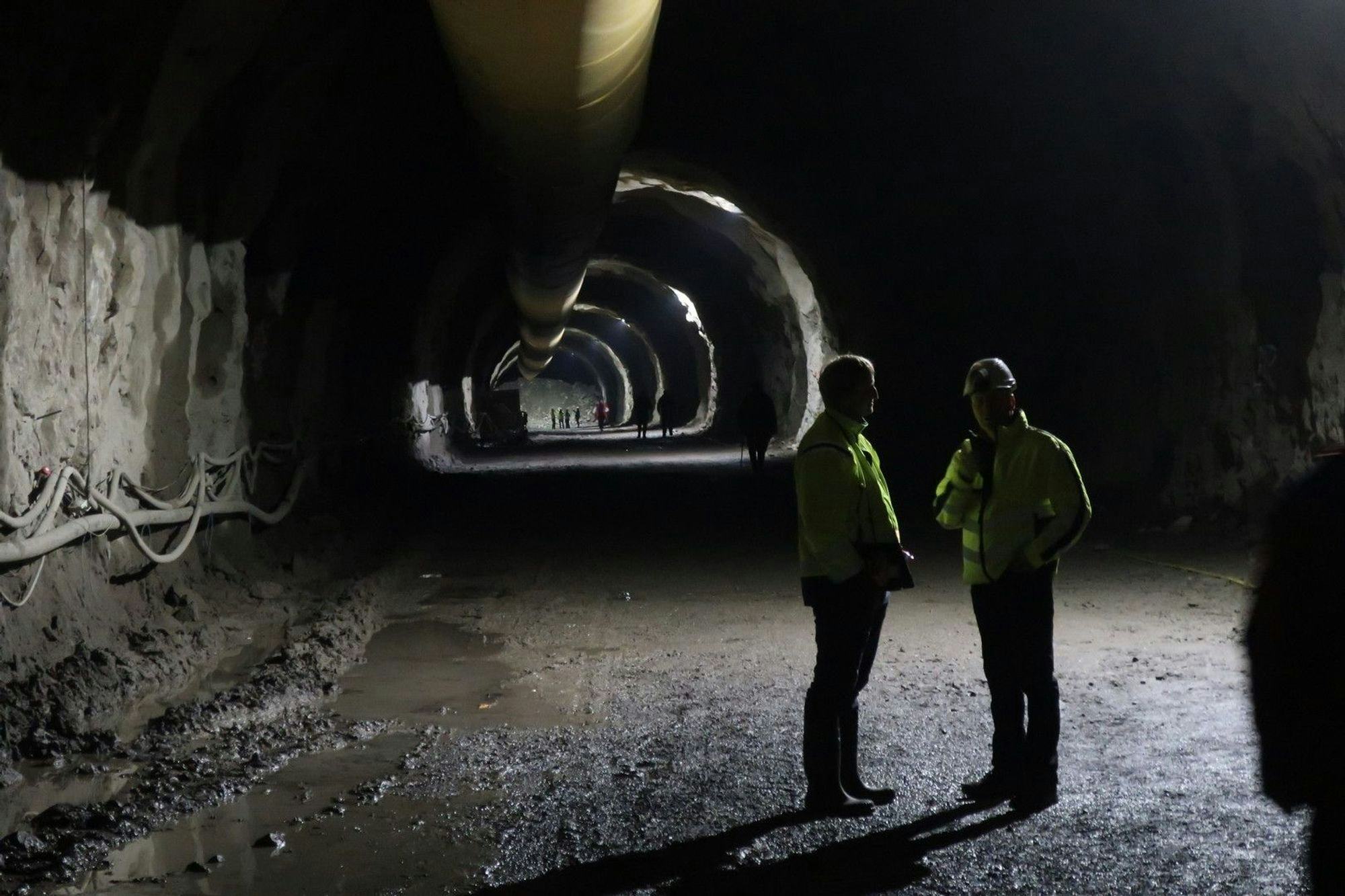 Two individuals in visibility jackets conversing in a large tunnel 